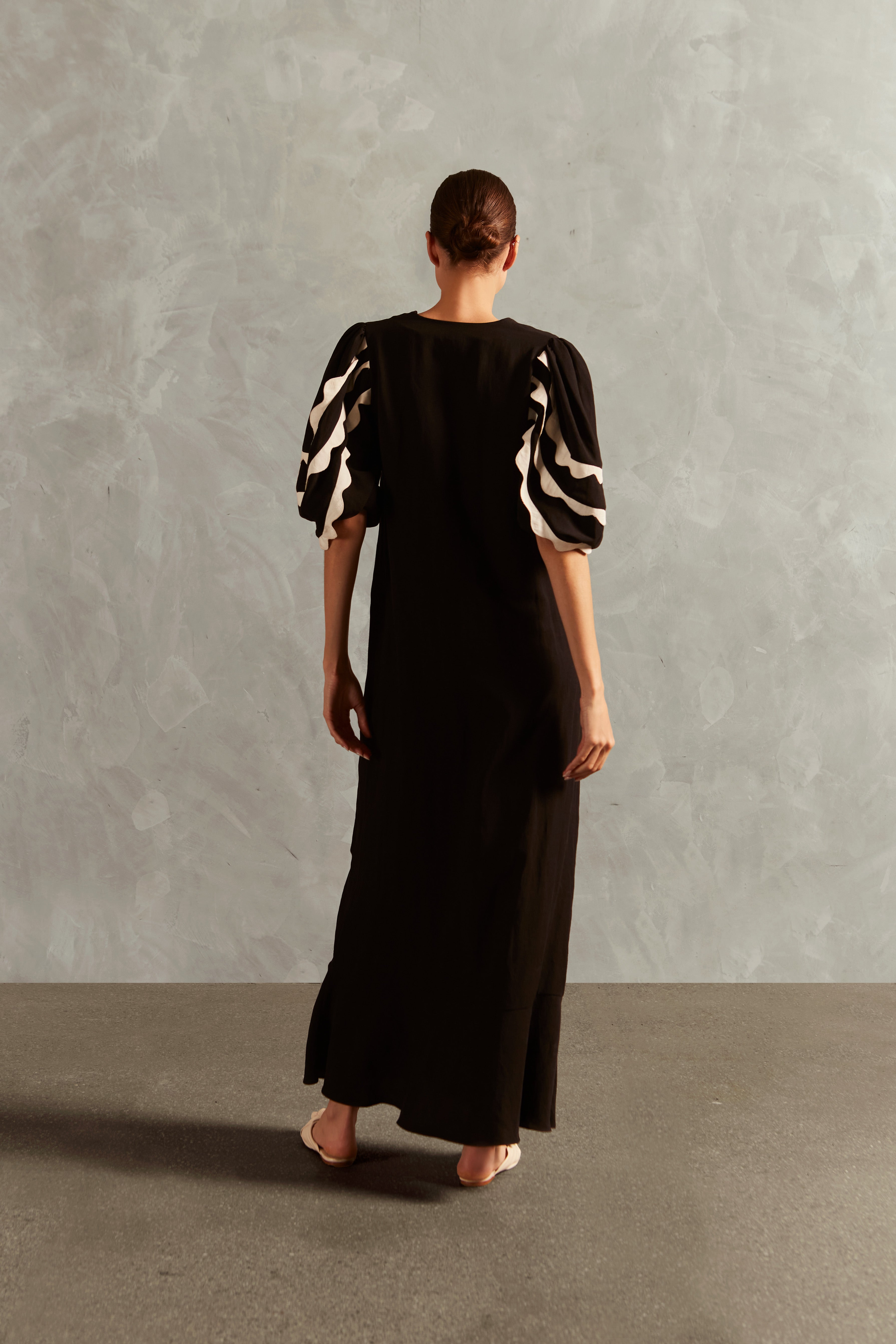 Model wearing the Appliqué V-Neck Long Dress Back showcasing its Black print on 55% Linen 45% Viscose fabric, styled for an afternoon look.