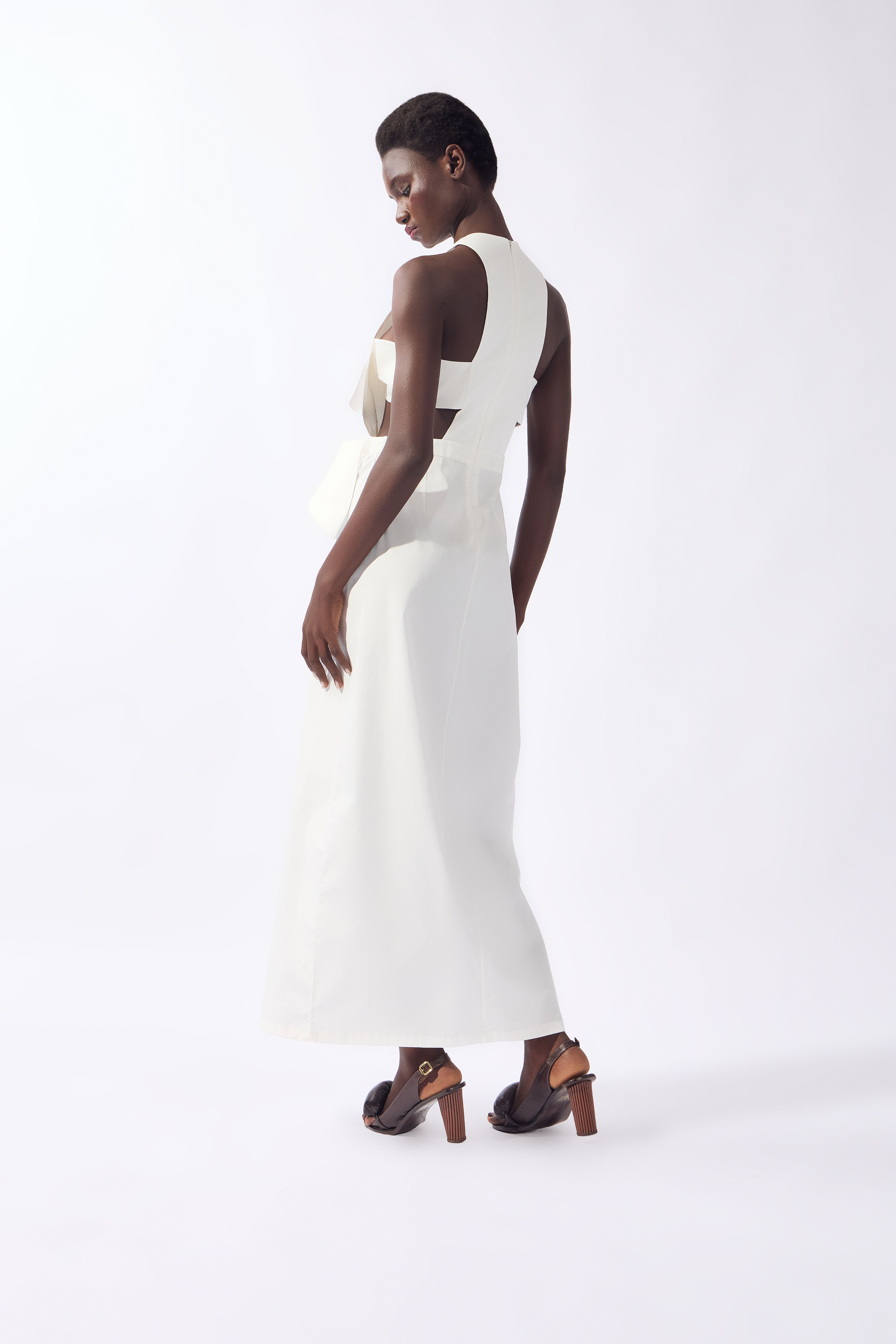 Model wearing the Bow Maxi Dress back color off white, made from 980% cotton 2% elastane, styled for a dinner look