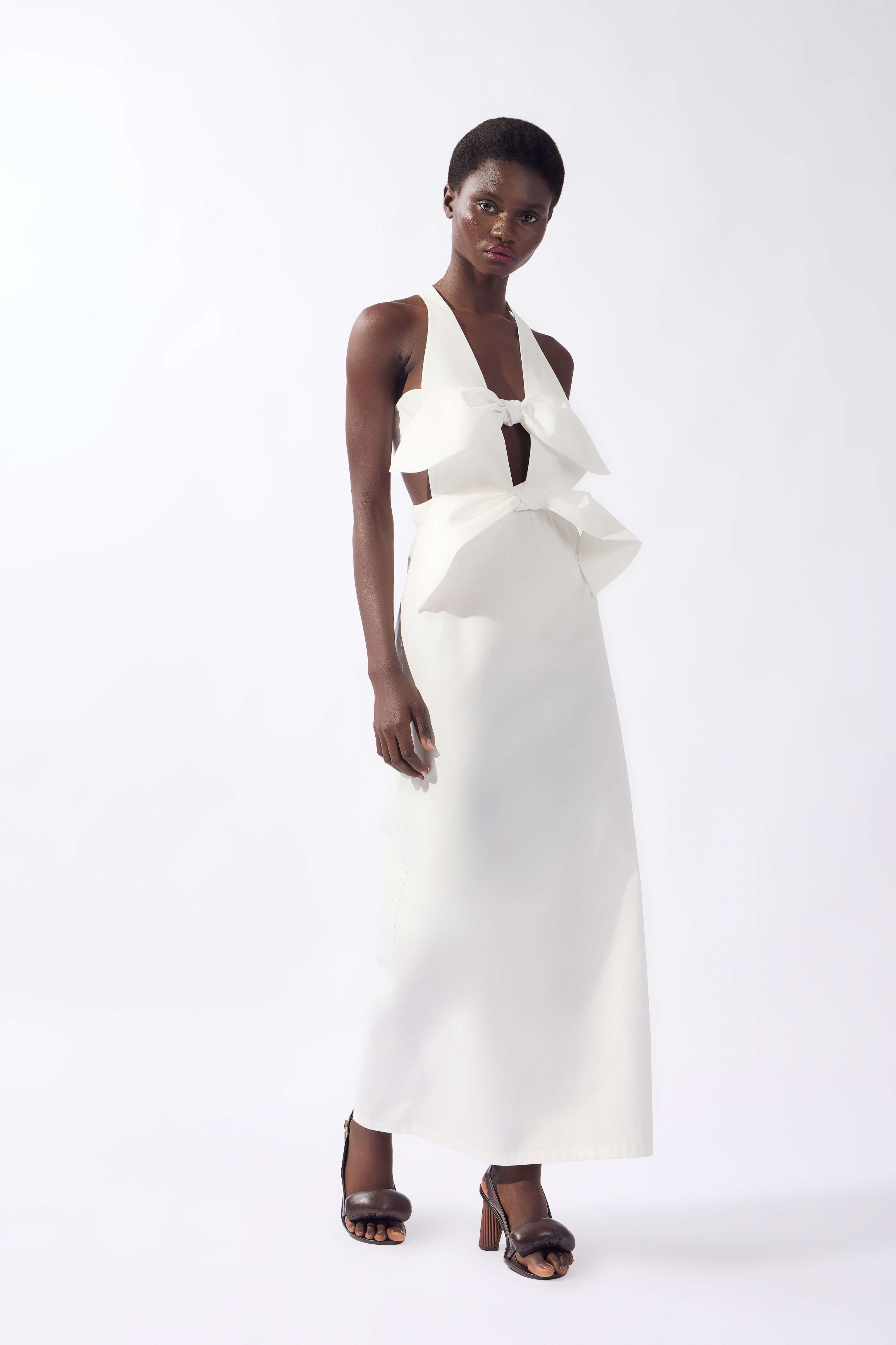Model wearing the Bow Maxi Dress front color off white, made from 980% cotton 2% elastane, styled for a dinner look