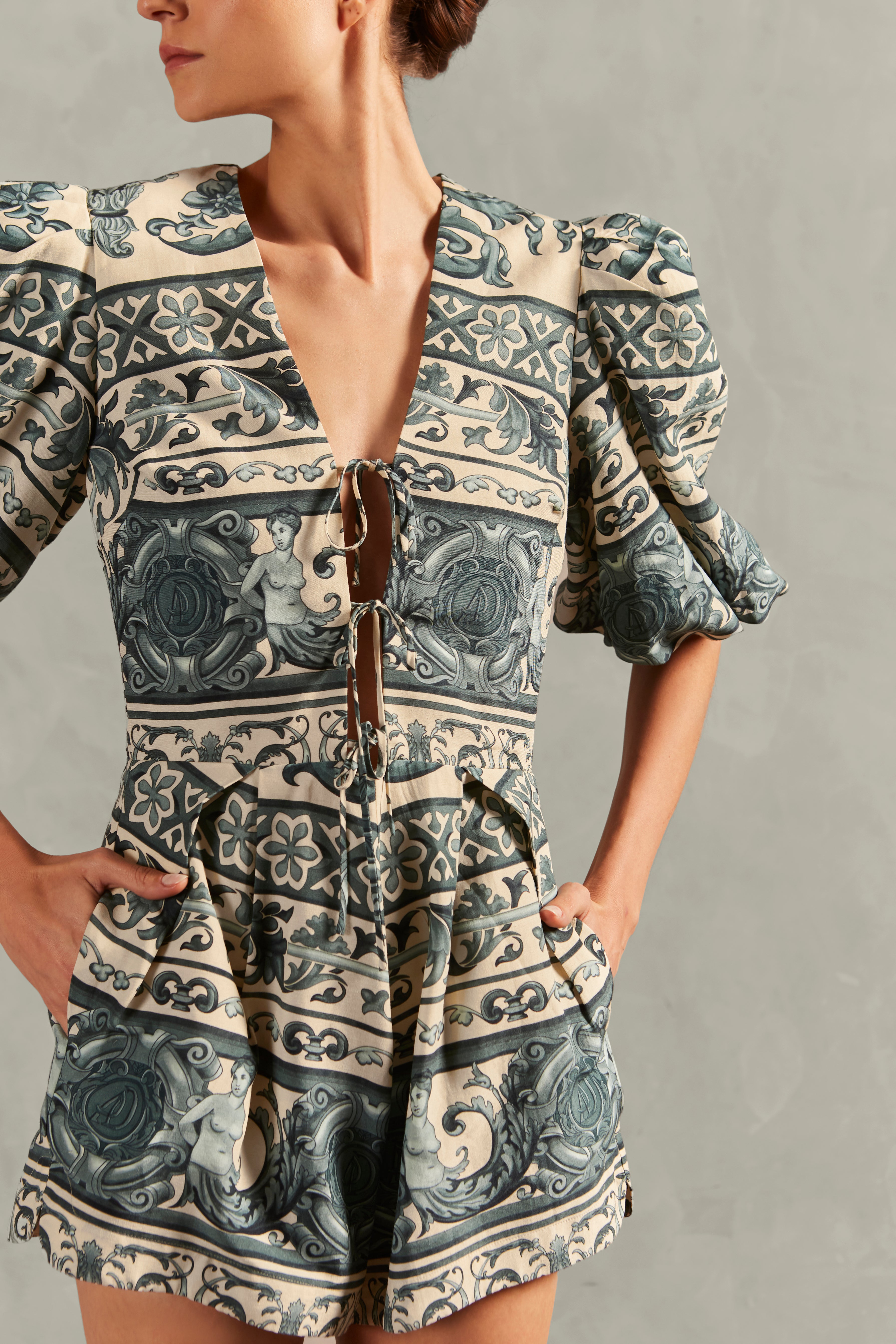 Model wearing the Hera V-Neck Playsuit Detail showcasing its BLUE color on 56% Viscose 24% Linen 20% Silk fabric, styled for a resort look.