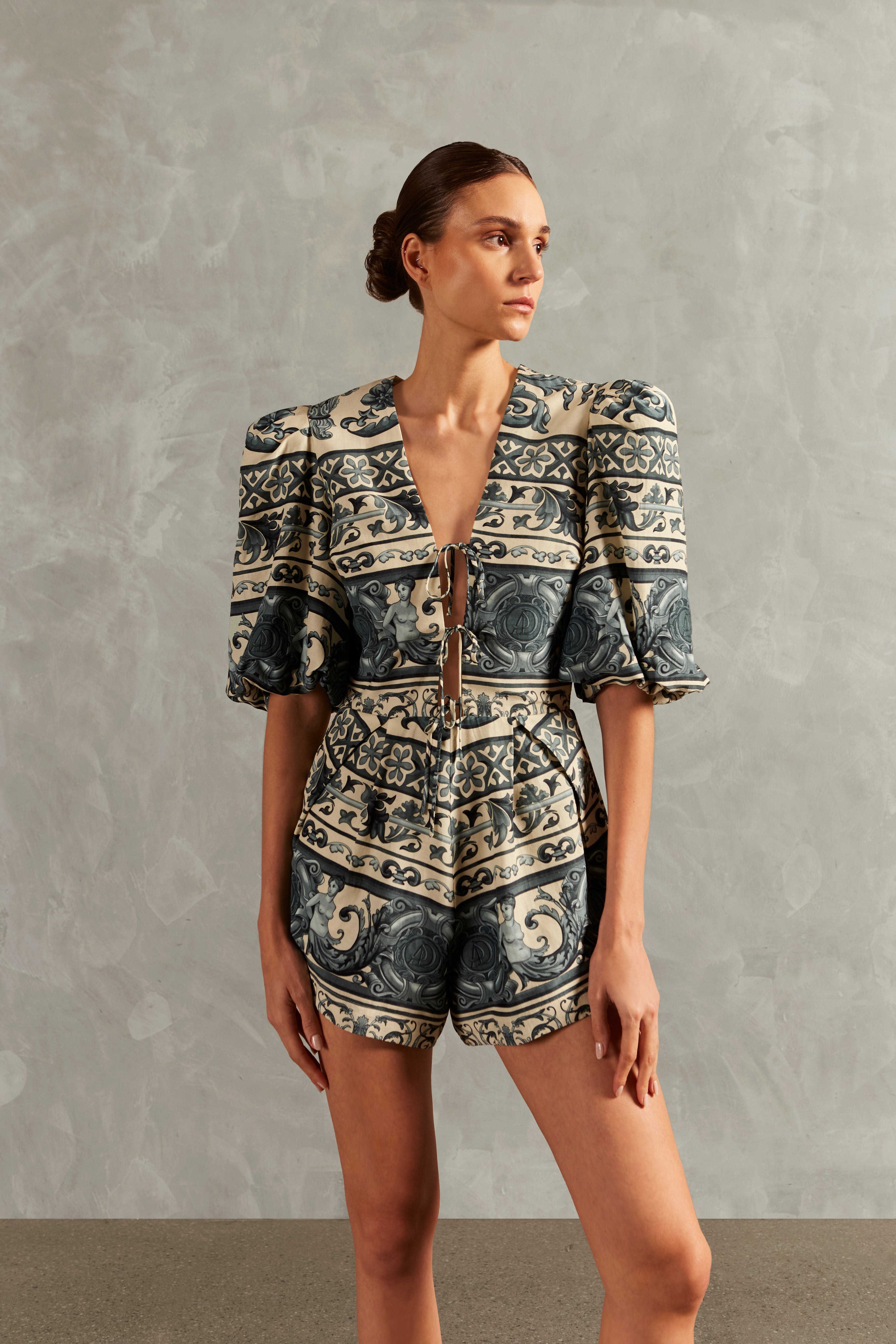 Model wearing the Hera V-Neck Playsuit Front showcasing its BLUE color on 56% Viscose 24% Linen 20% Silk fabric, styled for a resort look.