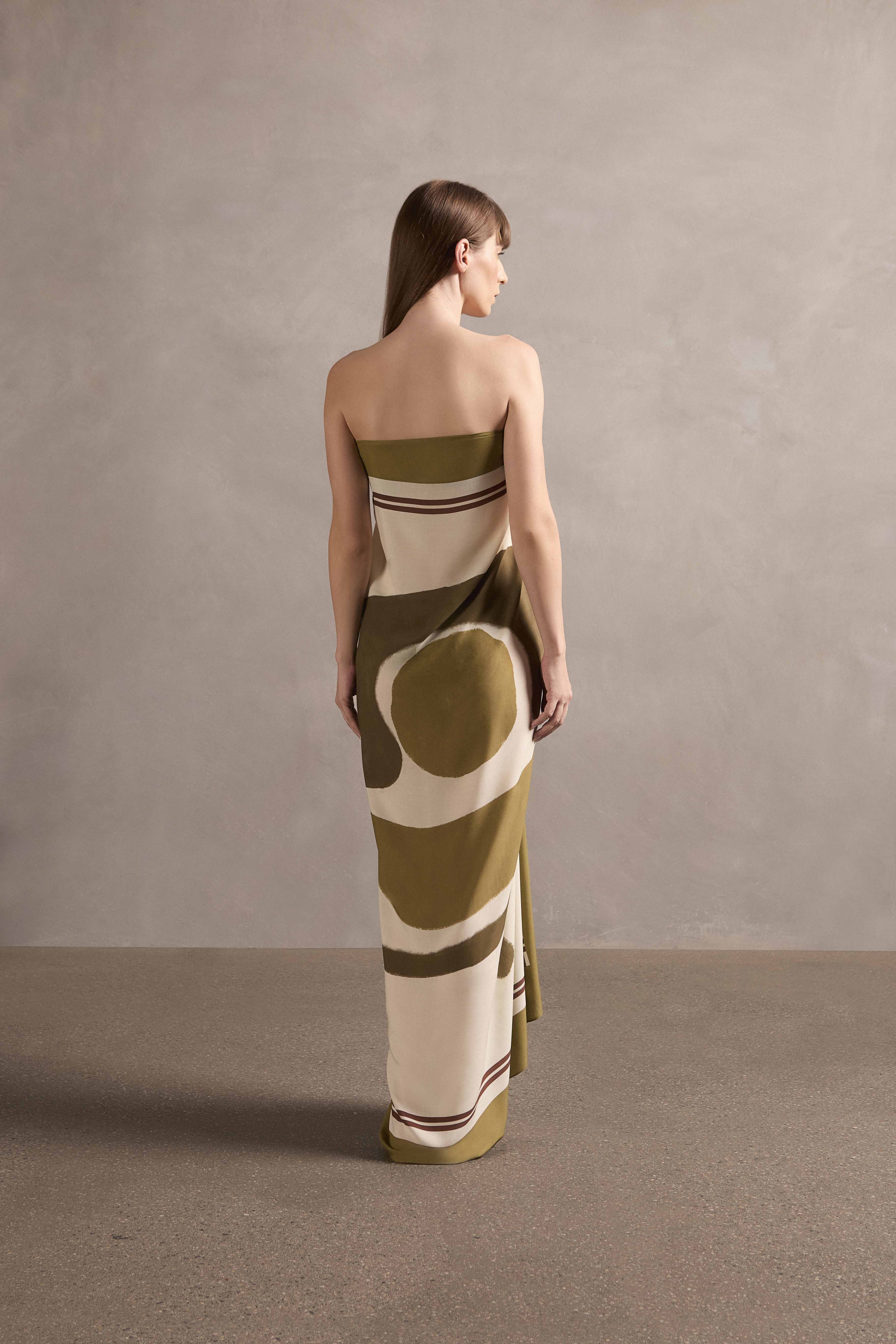 Model showcasing the back of the Mobile Lina Bo Bardi Panneaux showcasing its vintage references with green print on off-white 100% viscose fabric used as a dress, styled for a resort look.
