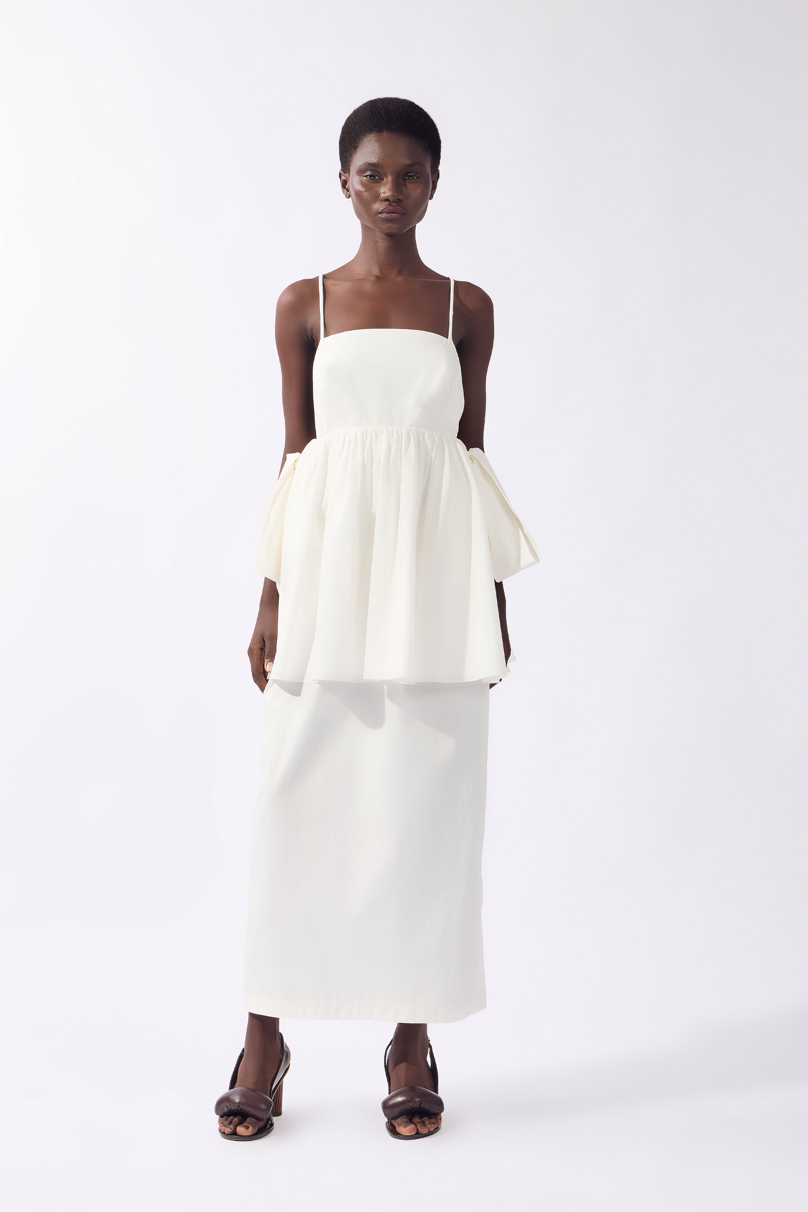 Model wearing the Peplum Maxi Dress front color off white, made from 98% cotton 2% elastane, styled for resort look