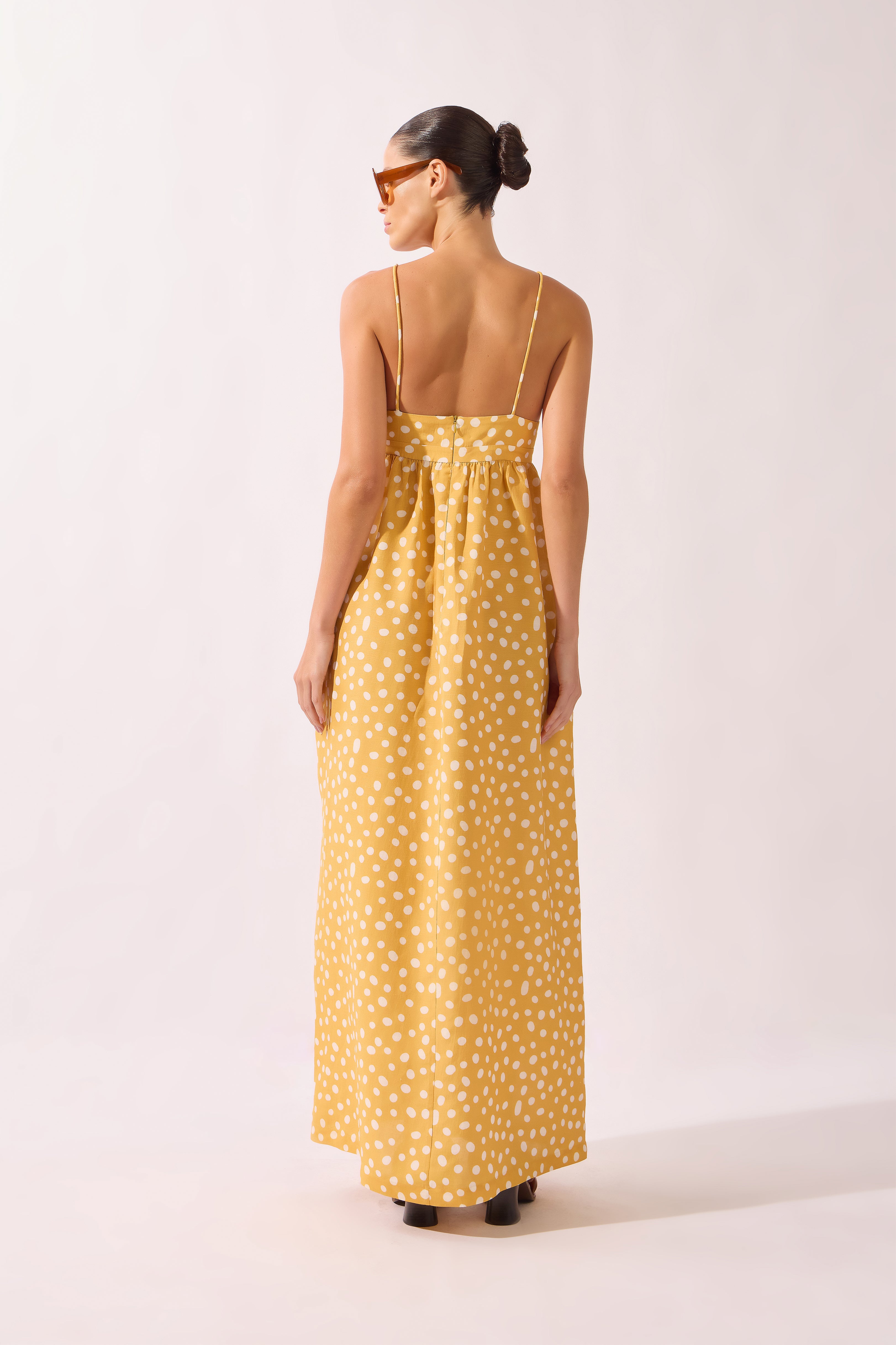 Model wearing the Polka Dots Maxi Dress back color cashew yellow, made from 55% linen 45% viscose, styled for a resort look