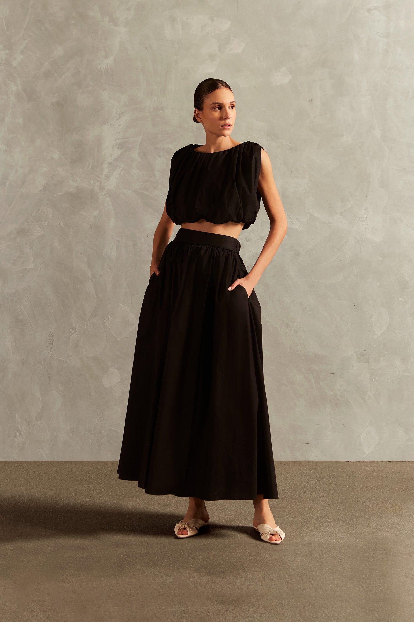 Model wearing the Solid Inamorata Side-Slit Long Skirt Front showcasing its Black color on 98% Cotton 2% Elastane fabric, styled for an afternoon look.
