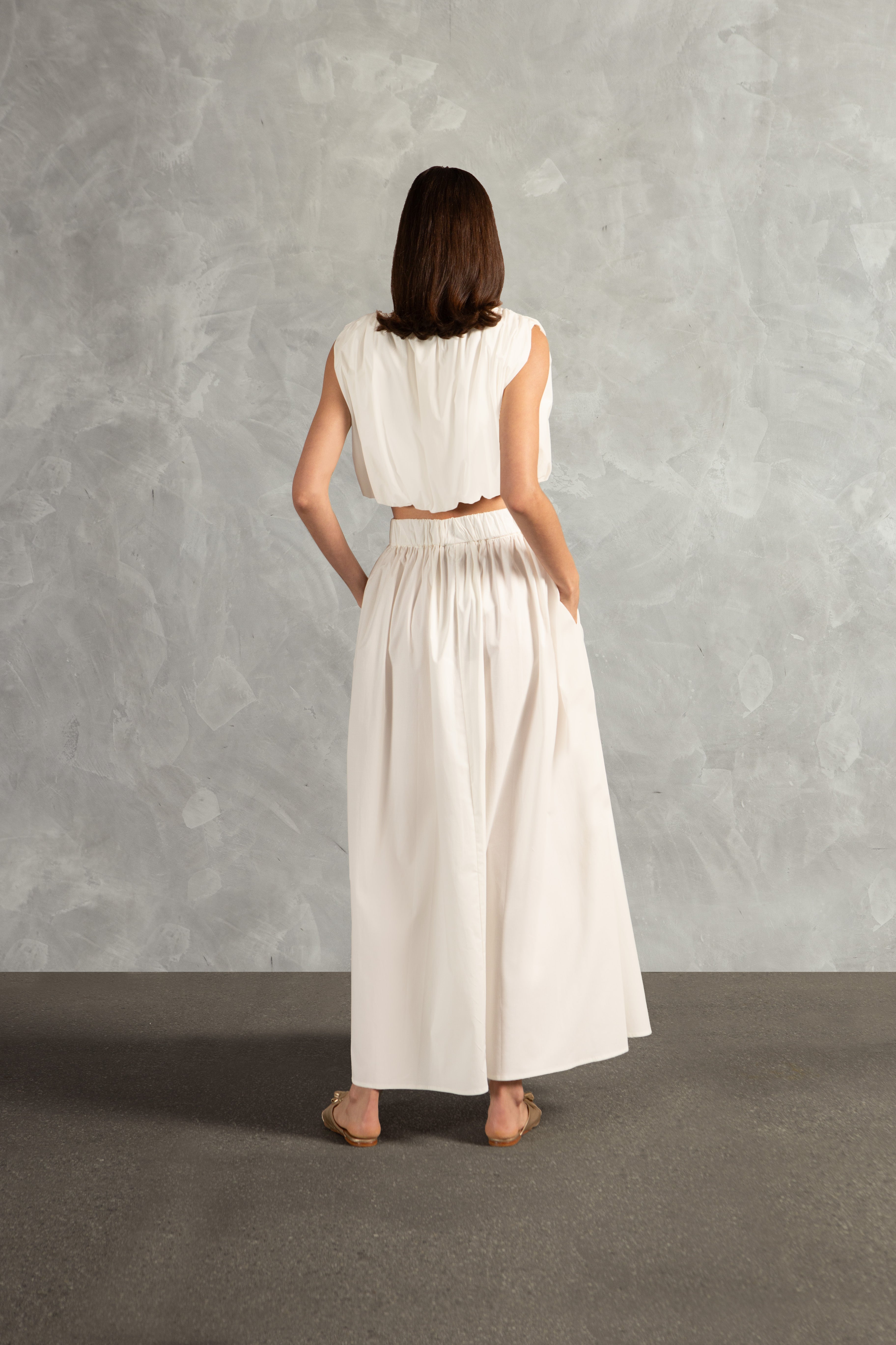 Model wearing the Solid Inamorata Side-Slit Long Skirt Back showcasing its Off White color on 98% Cotton 2% Elastane fabric, styled for an afternoon look.