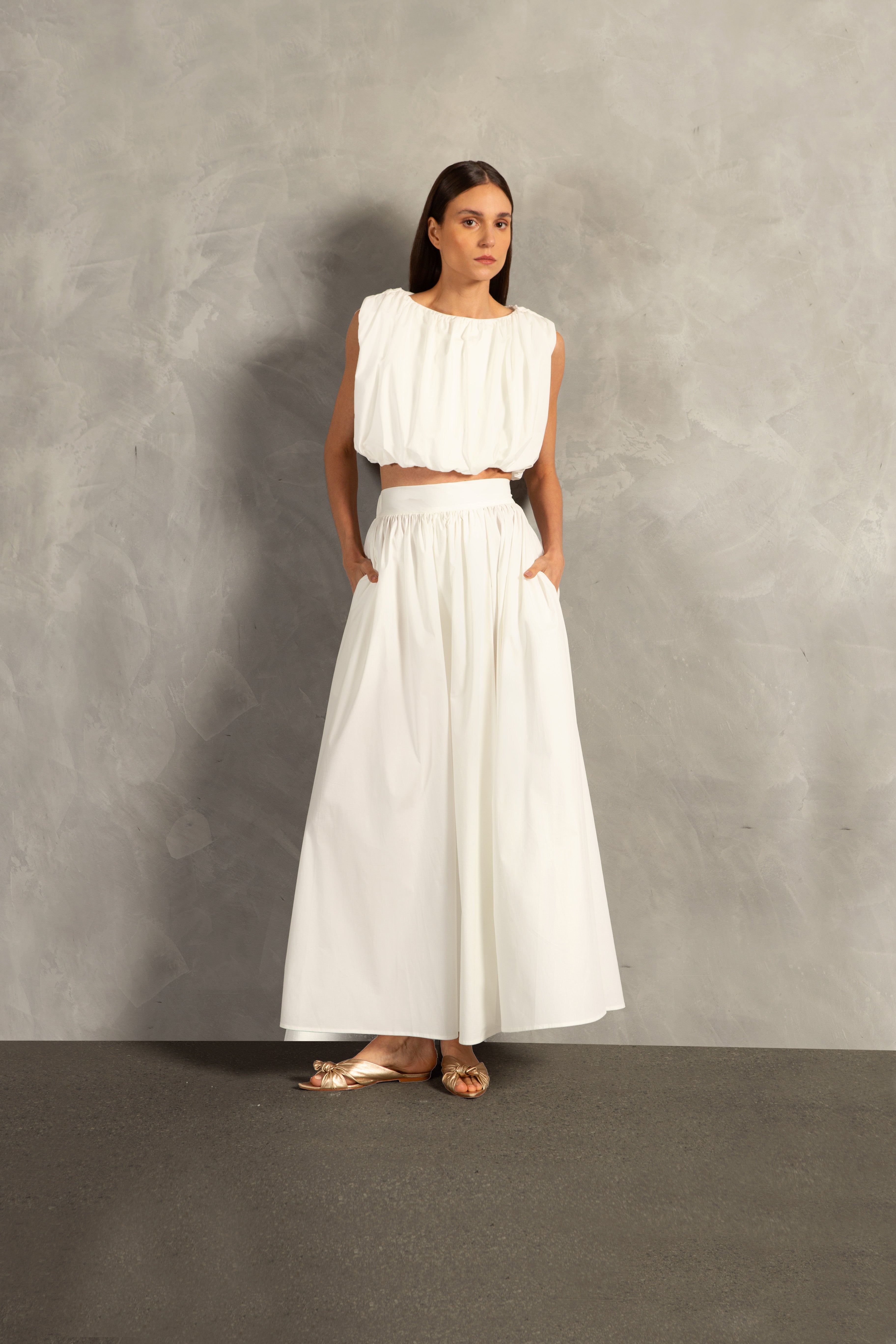 Model wearing the Solid Inamorata Side-Slit Long Skirt Front showcasing its Off White color on 98% Cotton 2% Elastane fabric, styled for an afternoon look.