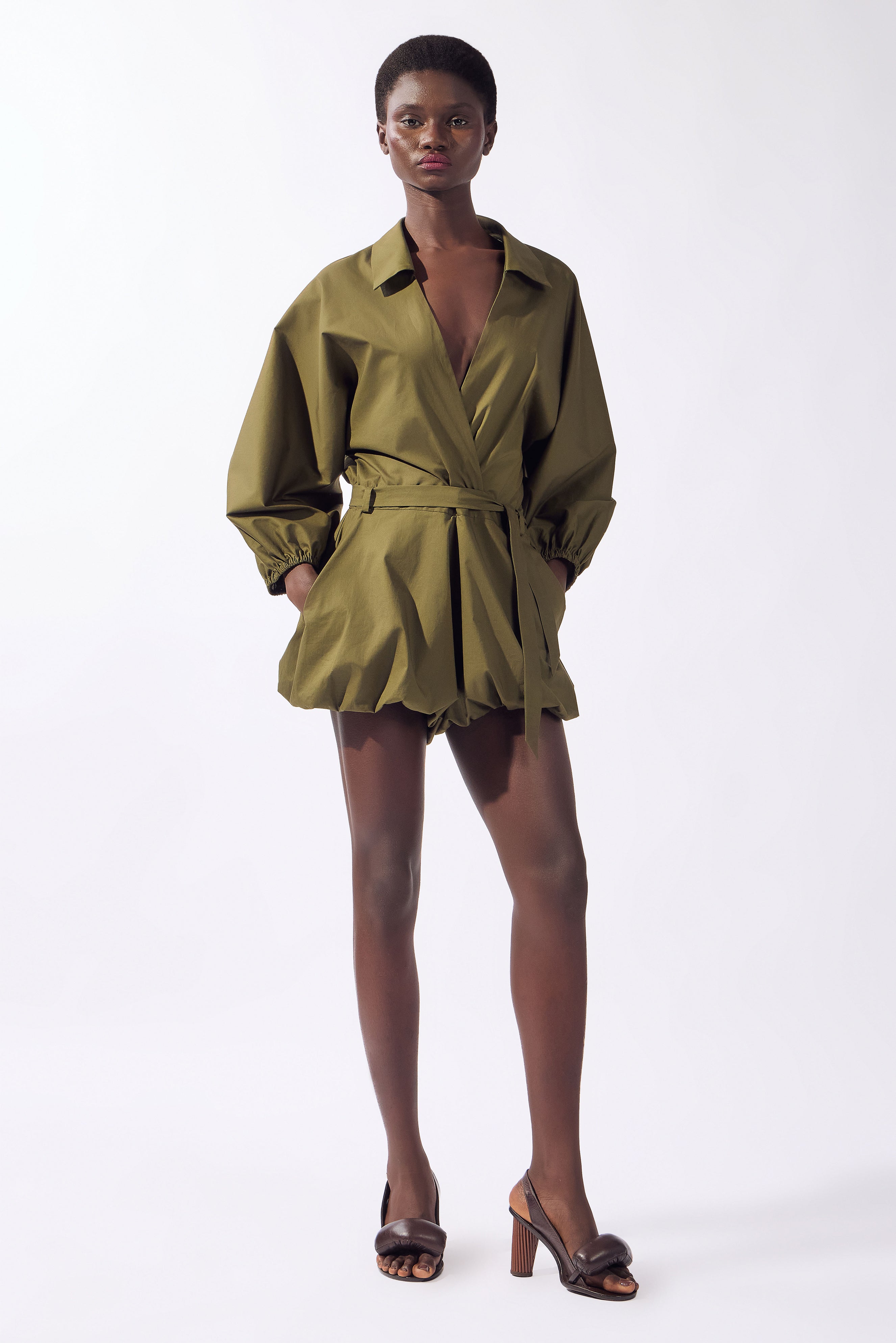 Model wearing the Solid Deep V-Neck Playsuit front, color green, made from 98% cotton 2% elastane, styled for a resort look