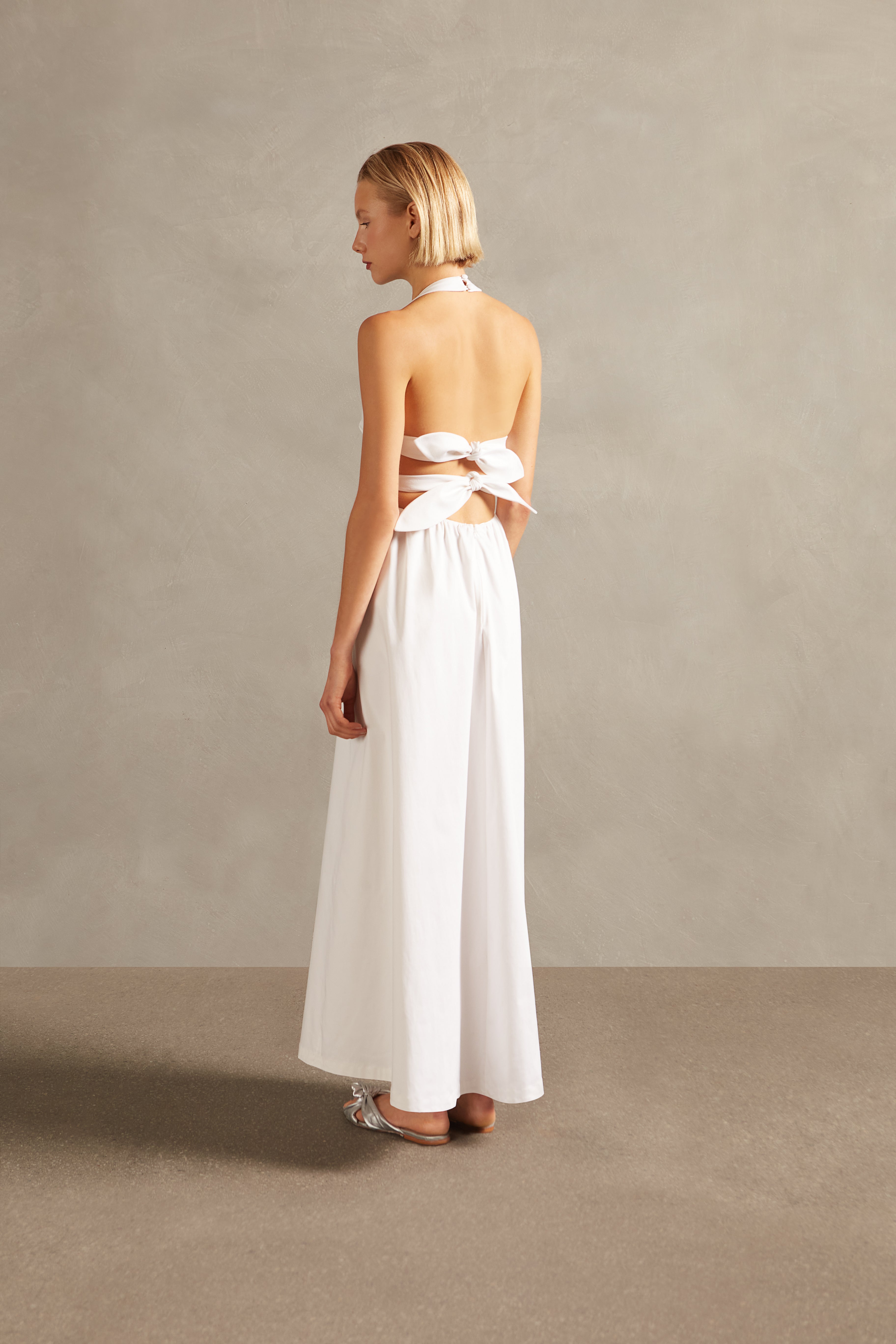 Model wearing the Solid Halter Long Dress off white back with 100% viscose, styled for a resort look.