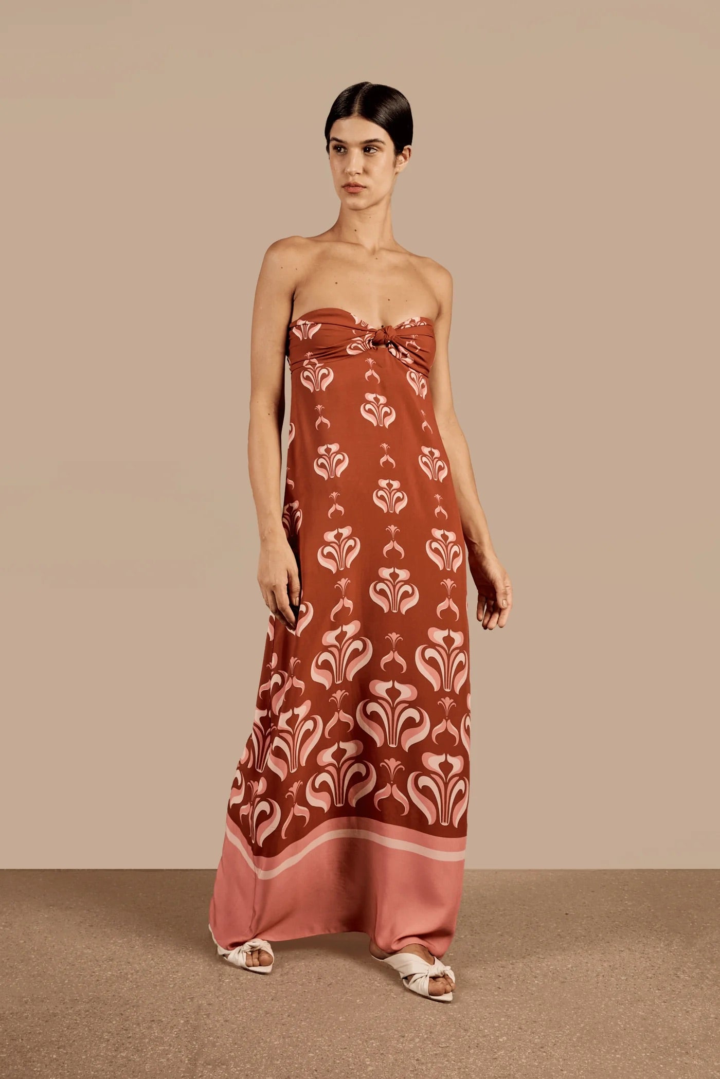 Model wearing the Vintage Lily Long Dress With Knot Detail showcasing the front of it's strapless design, with dark red and pink print, on a viscose fabric.
