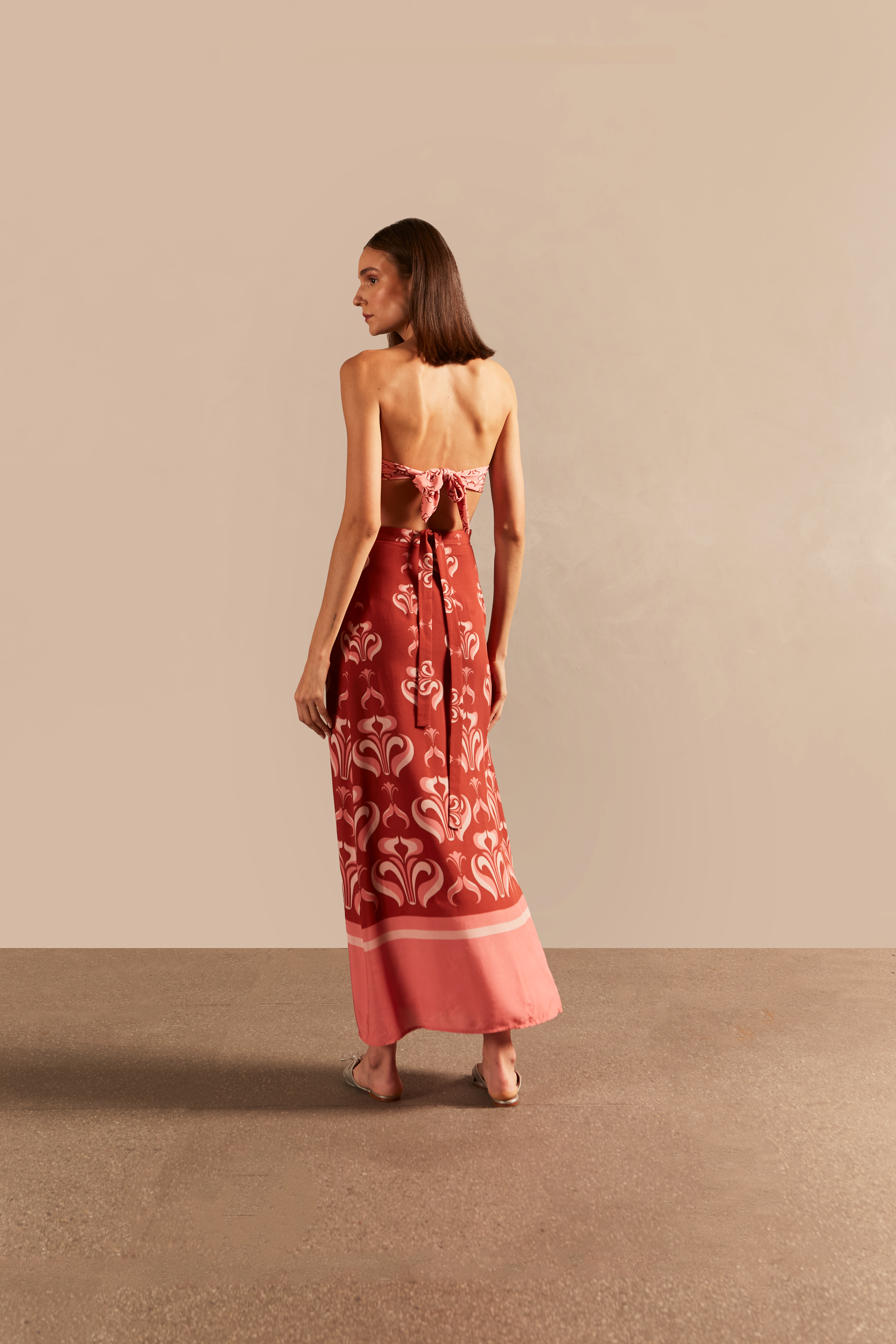 Model wearing the Vintage Lily Pareo Skirt showcasing the back of it's vintage-inspired dark red and pink print, on a viscose fabric.