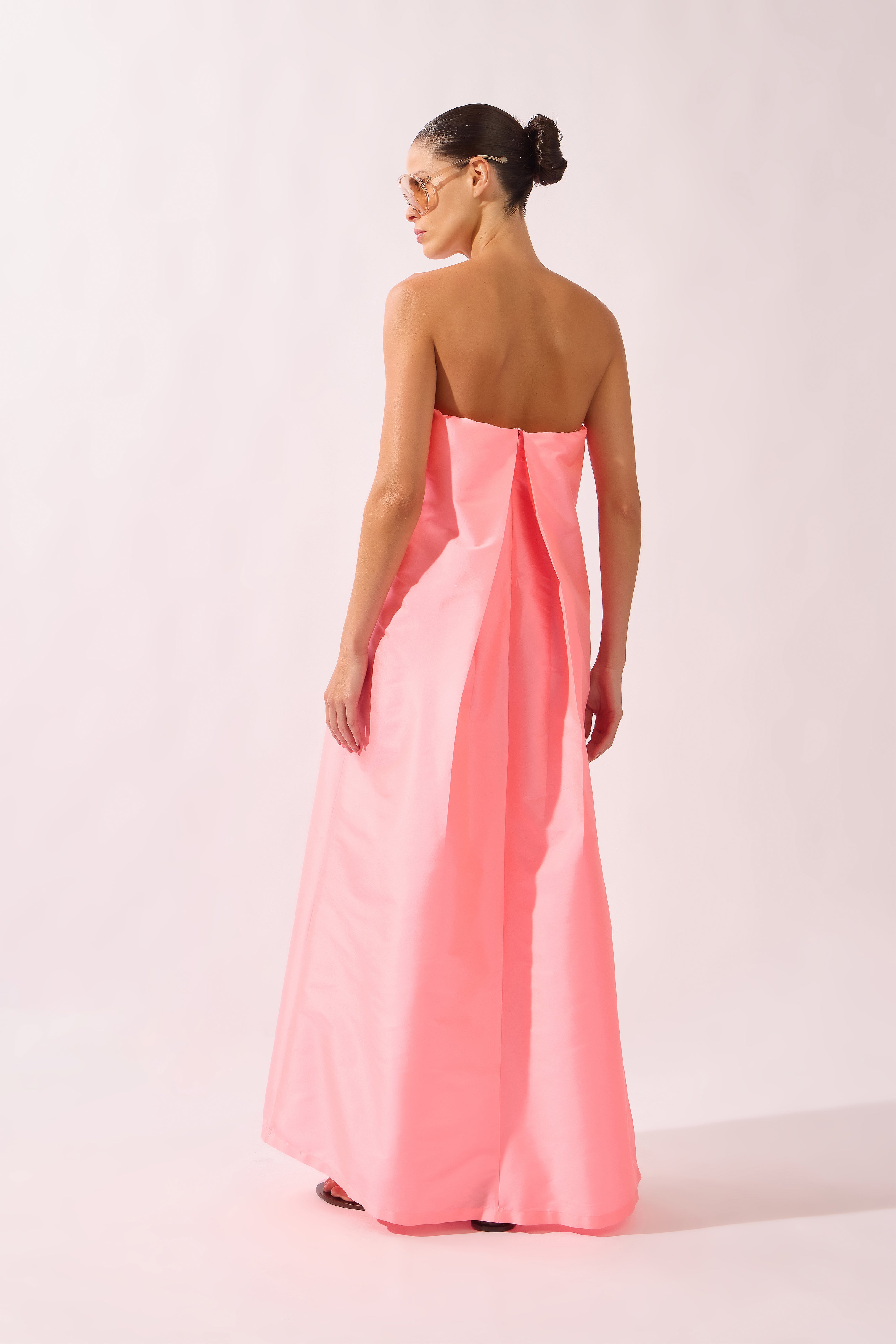 Model wearing the Voluminous Maxi Dress back color flourescent pink made with 100% polyetser, styled for an evening look