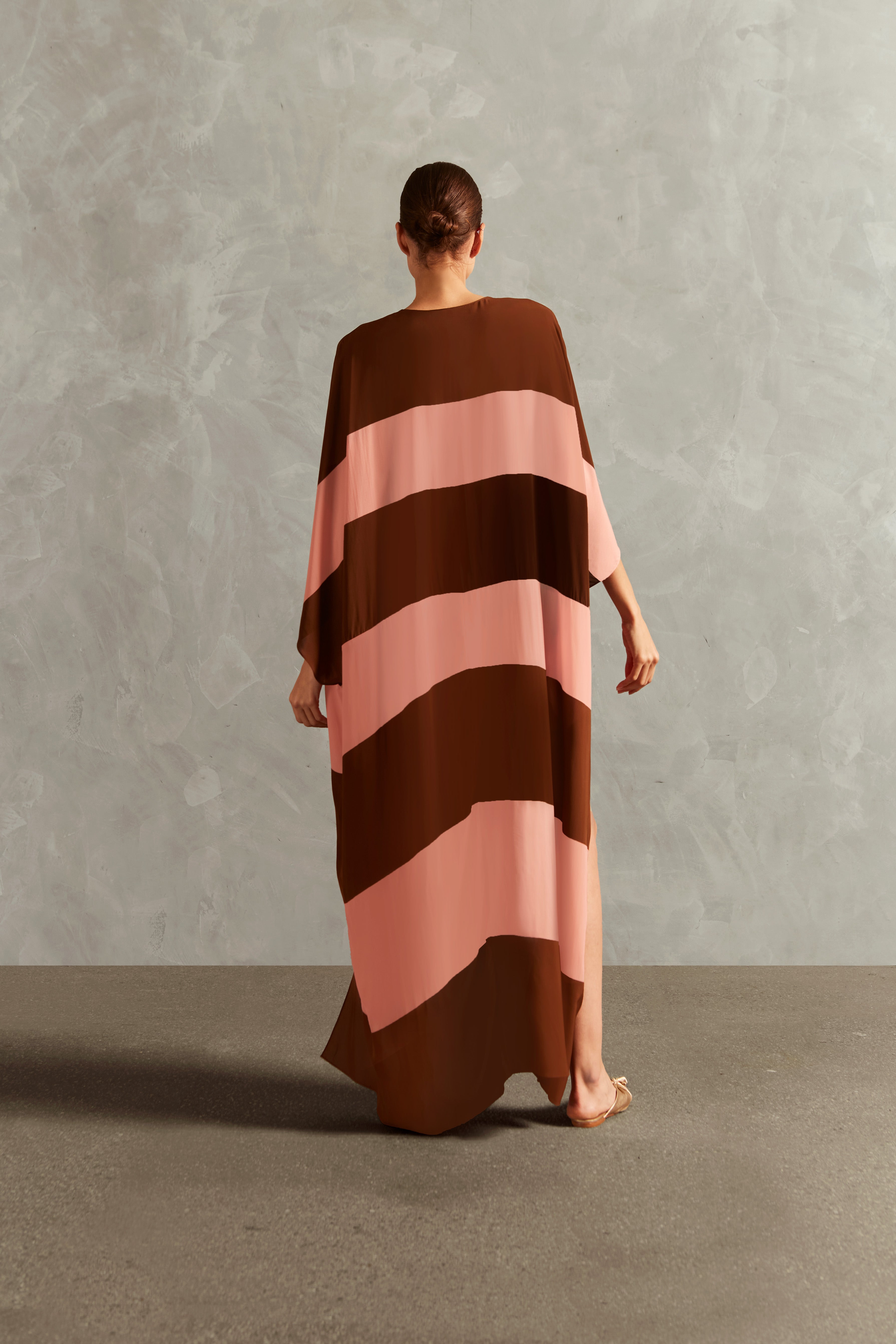 Model wearing the Bold Stripes Long Kaftan Back showcasing its Brown and Pink print on 100% Viscose fabric, styled for an post-beach look.