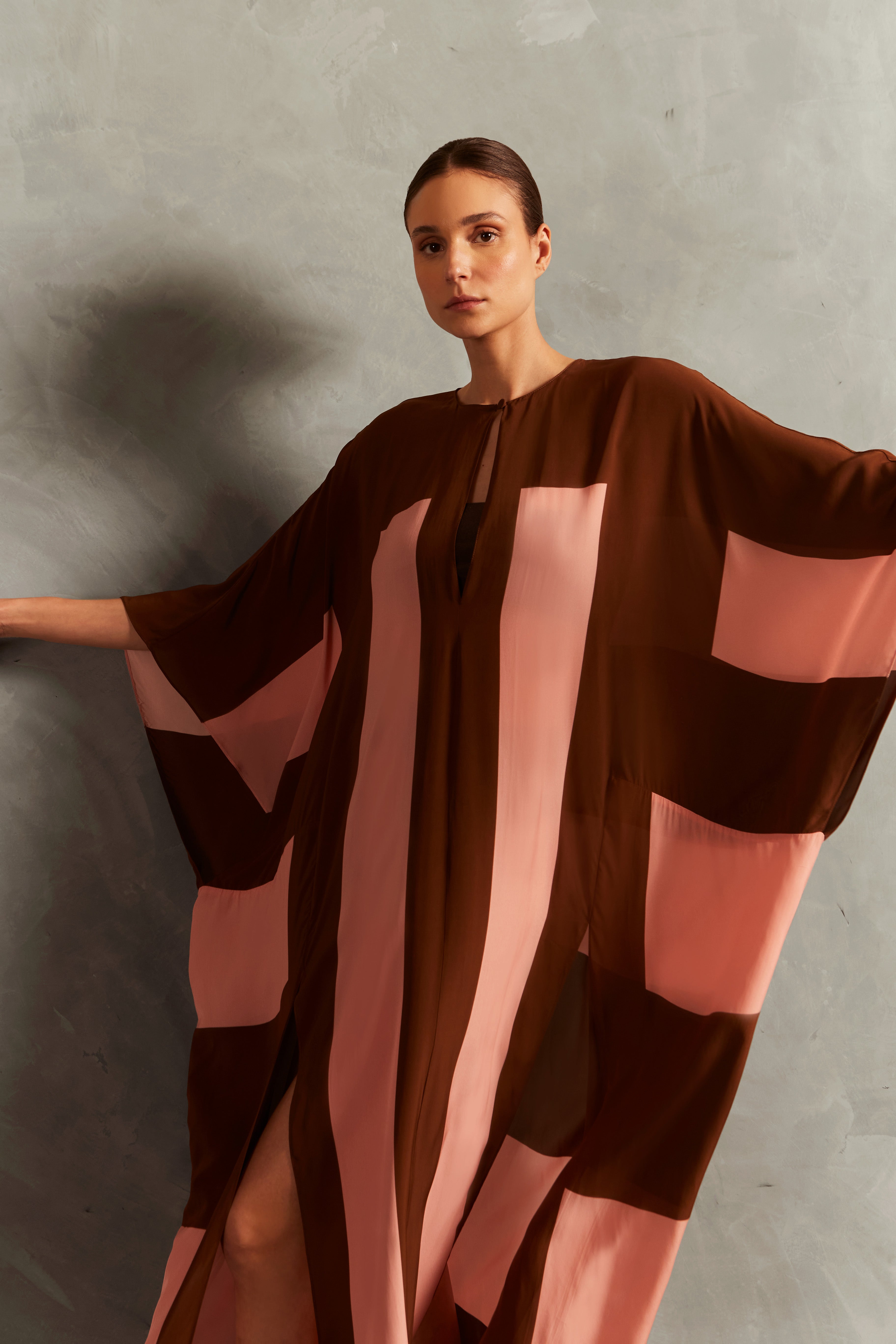 Model wearing the Bold Stripes Long Kaftan Detail showcasing its Brown and Pink print on 100% Viscose fabric, styled for an post-beach look.