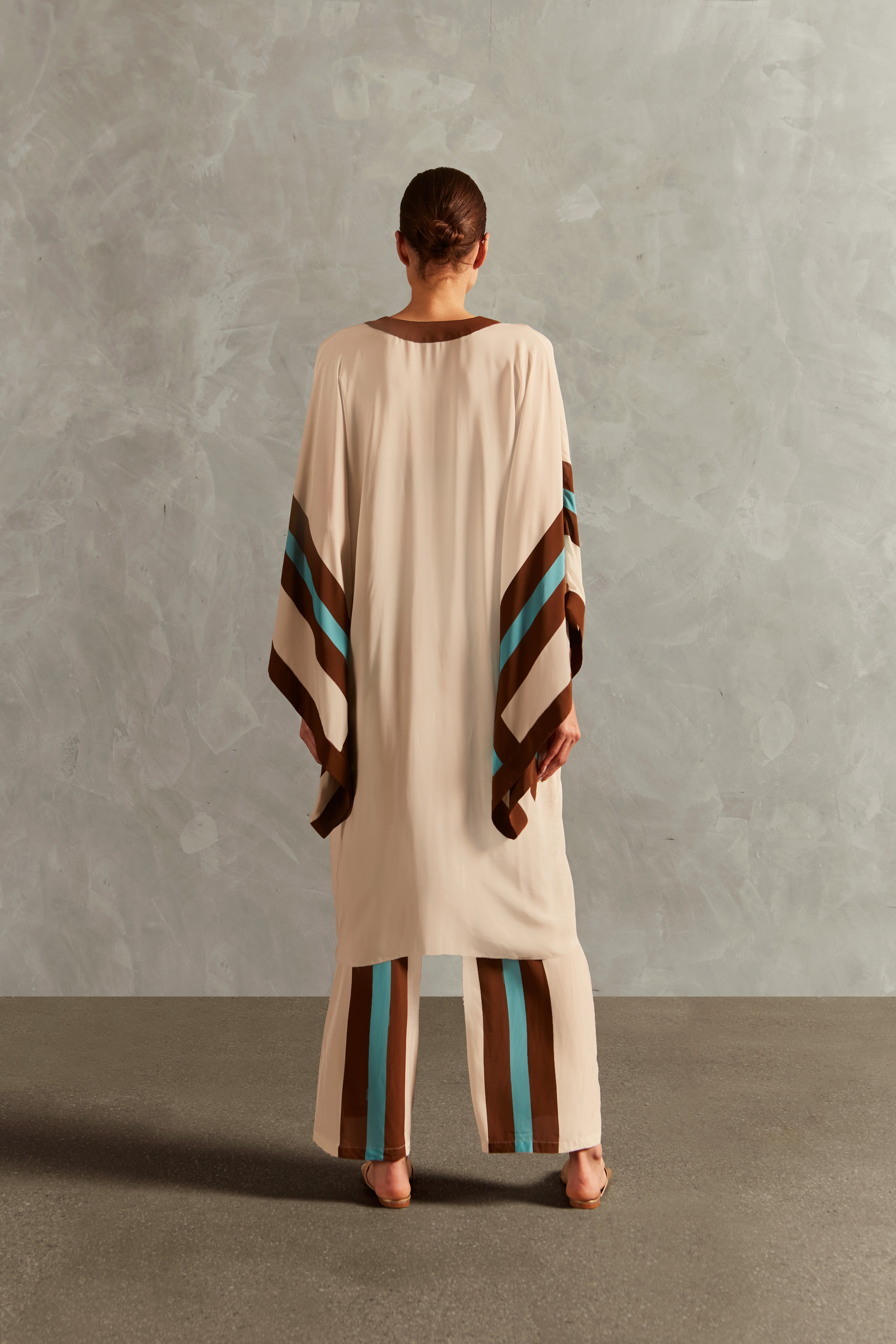 Model wearing the Bold Stripes Maxi Short Robe Back showcasing its Off White, Brown, Turquoise and Blue print on 100% Viscose fabric, styled for an afternoon look.