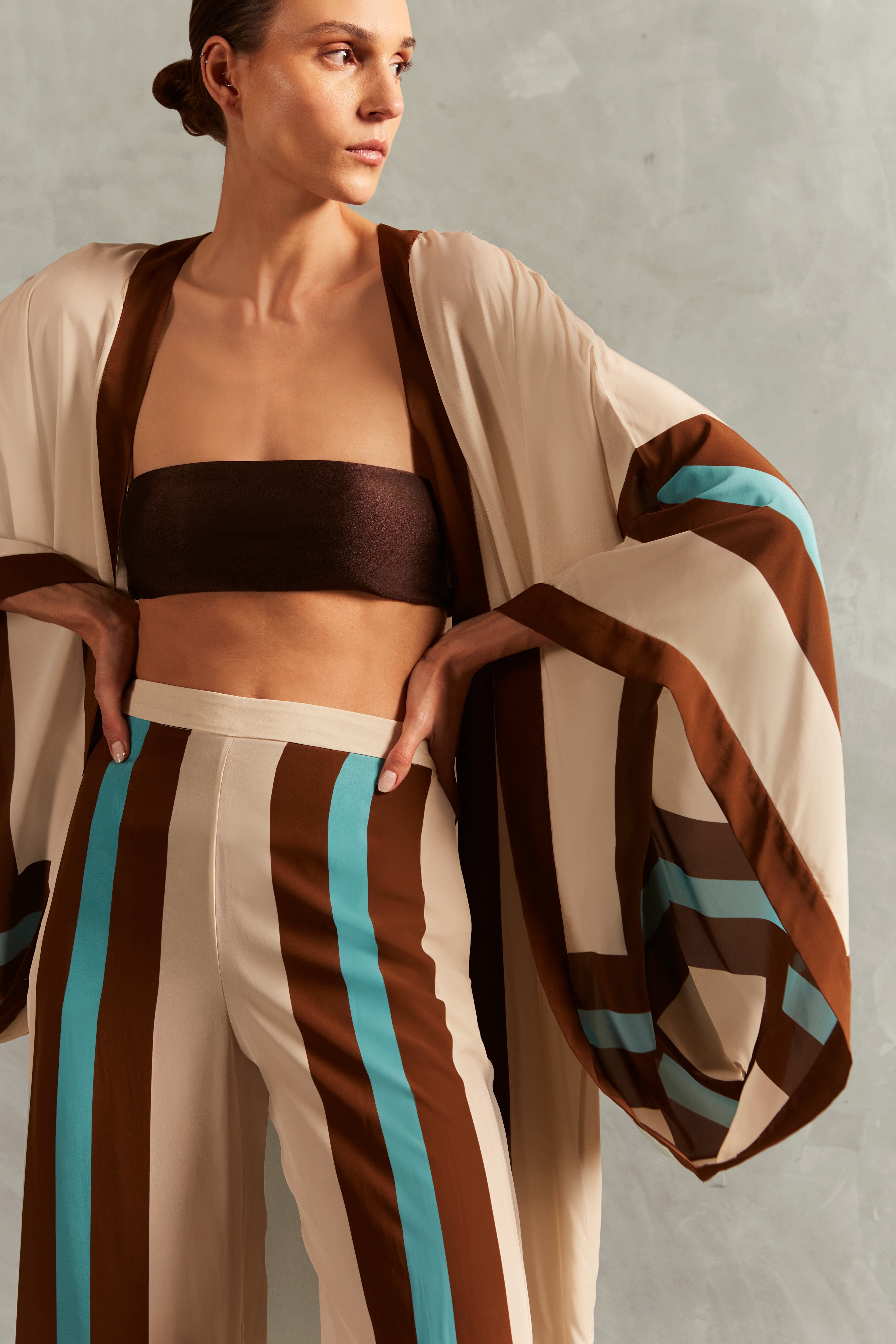 Model wearing the Bold Stripes Maxi Short Robe Detail showcasing its Off White, Brown, Turquoise and Blue print on 100% Viscose fabric, styled for an afternoon look.