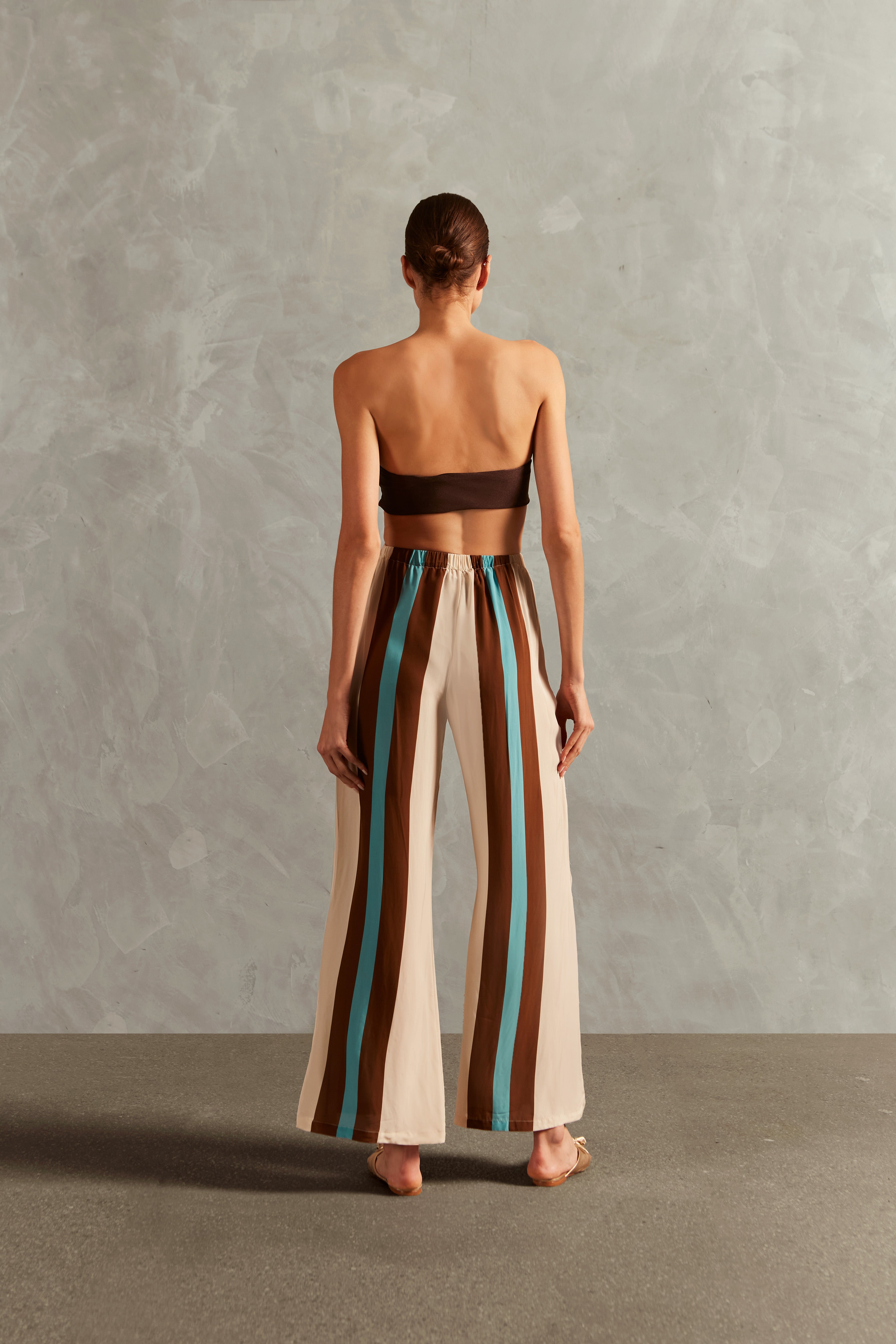 Model wearing the Bold Stripes Wide-Leg Pants Back  showcasing its Off White/Brown/Turquoise Blue print on 100% Viscose fabric, styled for an afternoon look.