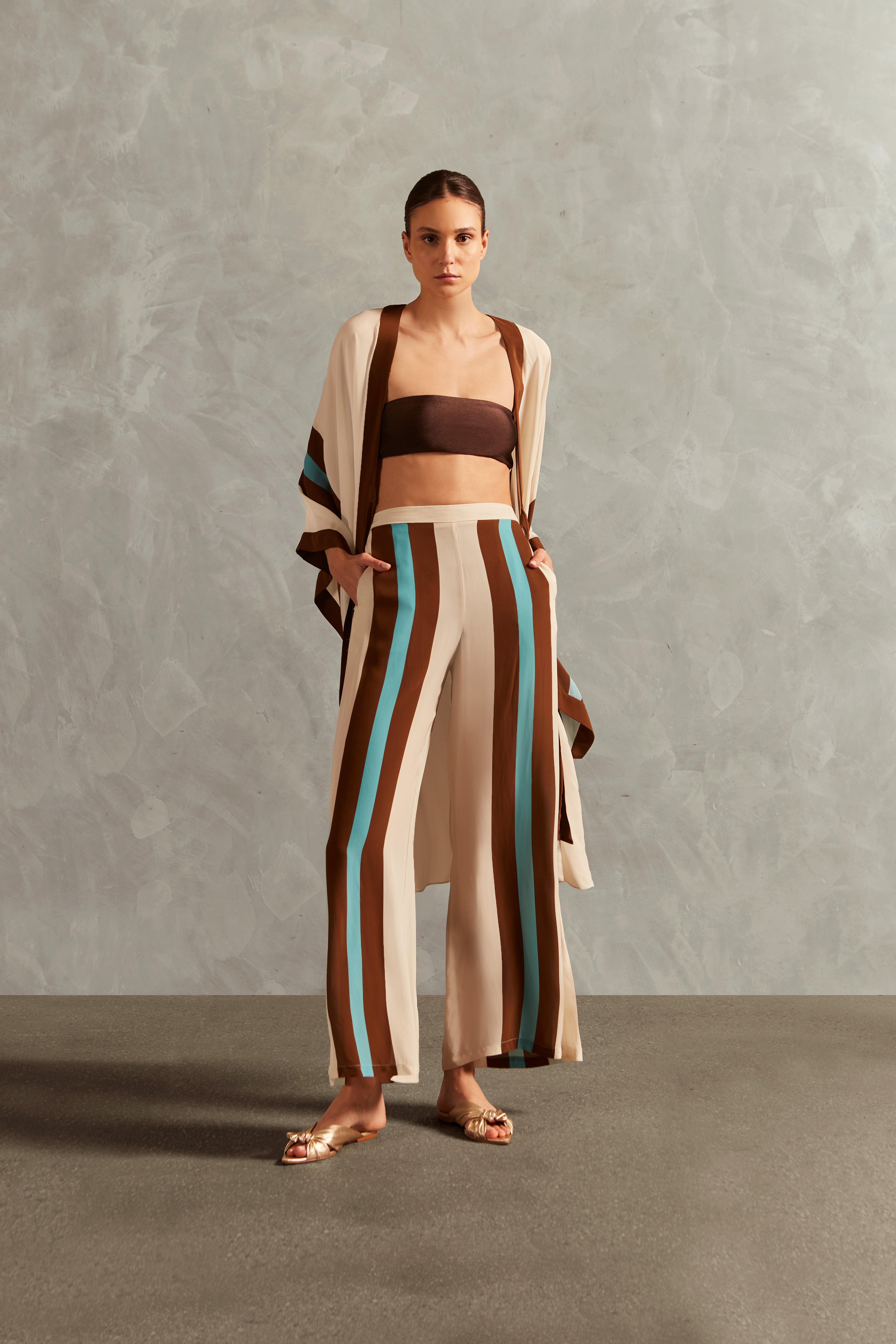 Model wearing the Bold Stripes Wide-Leg Pants Front showcasing its Off White/Brown/Turquoise Blue print on 100% Viscose fabric, styled for an afternoon look.