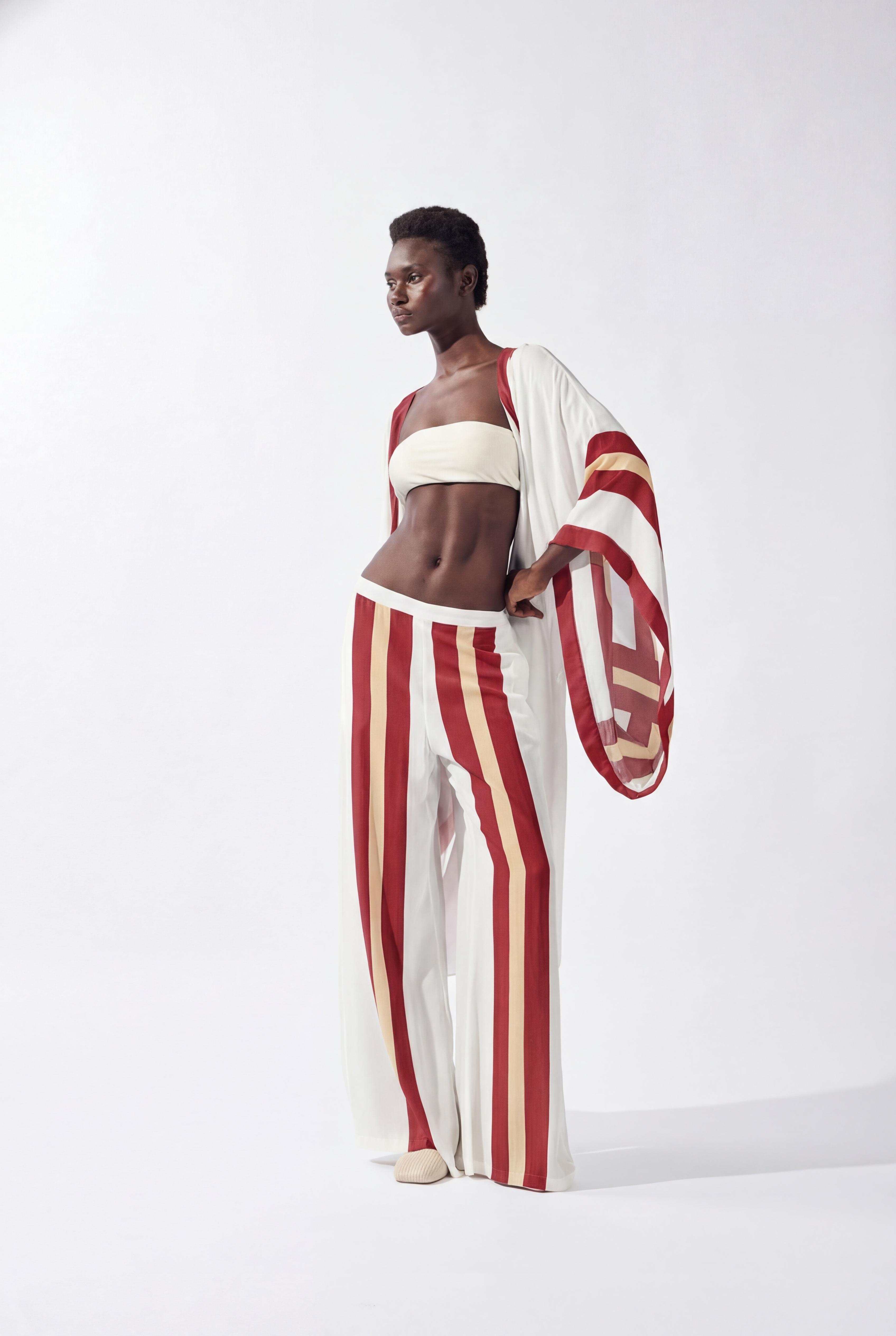 Model wearing the Bold Stripes Wide-Leg Pants look, color off white, burgundy, beige, made from 100% viscose, styled for a resort look