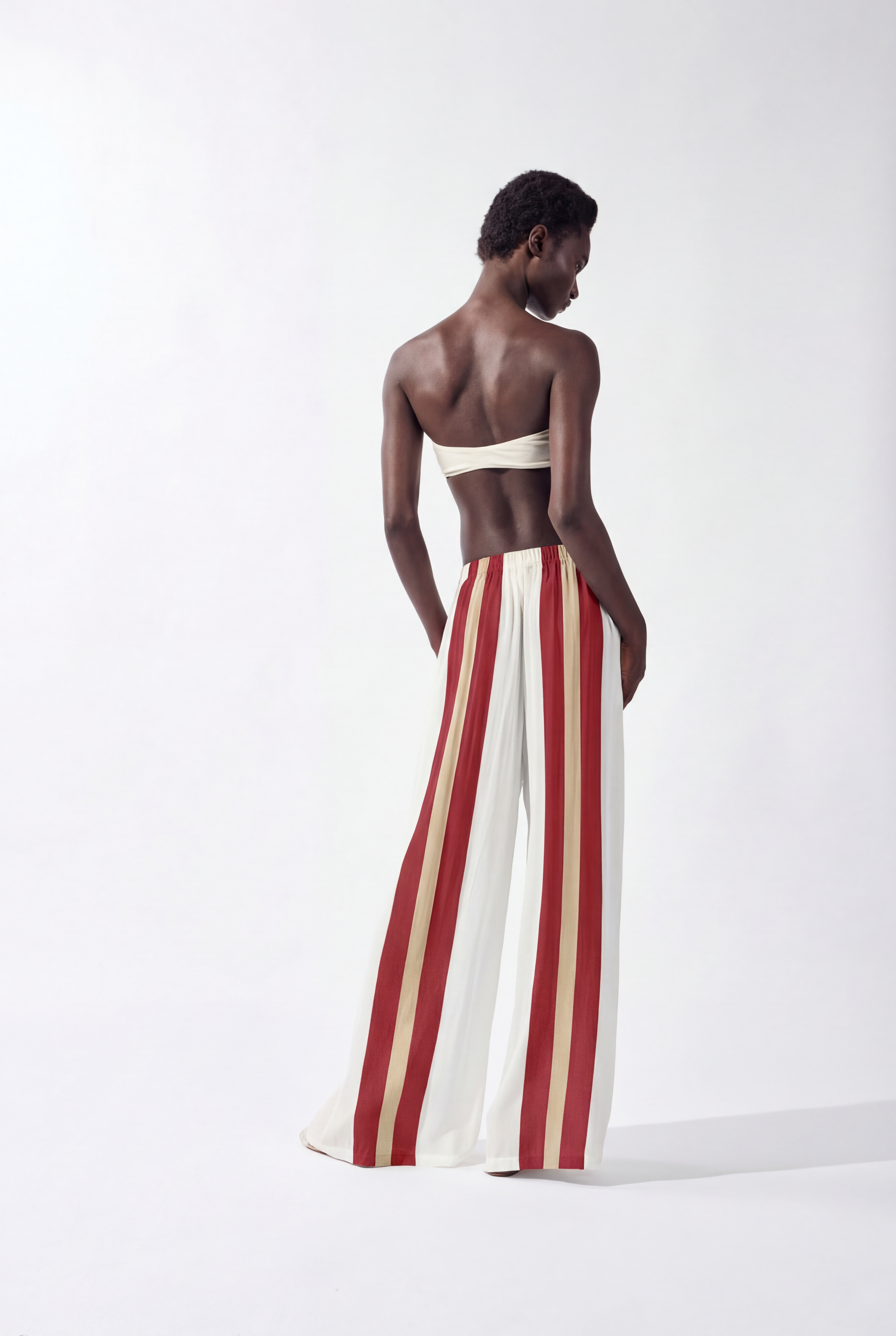 Model wearing the Bold Stripes Wide-Leg Pants back, color off white, burgundy, beige, made from 100% viscose, styled for a resort look