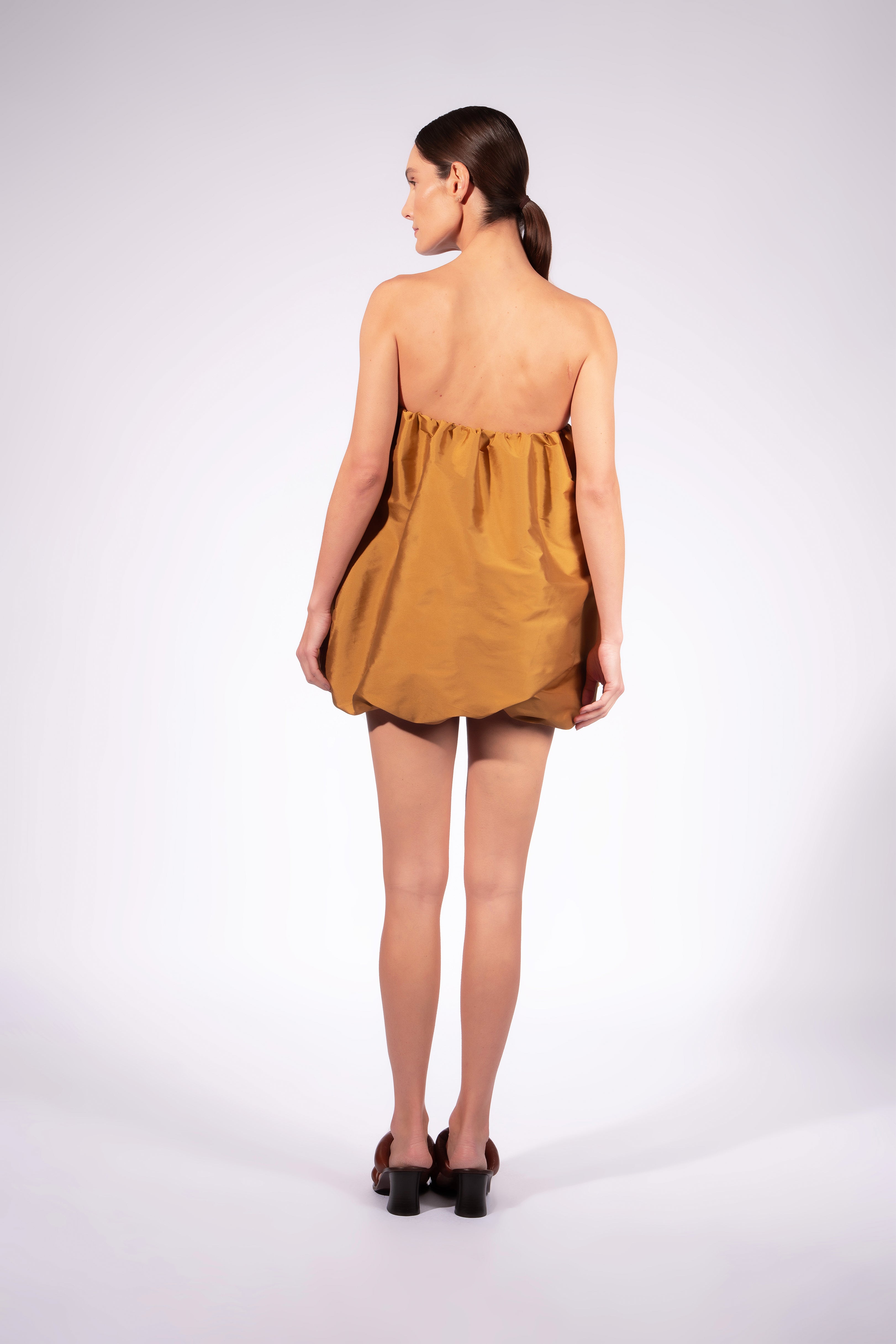 Model wearing the Bubble Spiral Dress back color ochre made with 100% polyetser, styled for an night out look