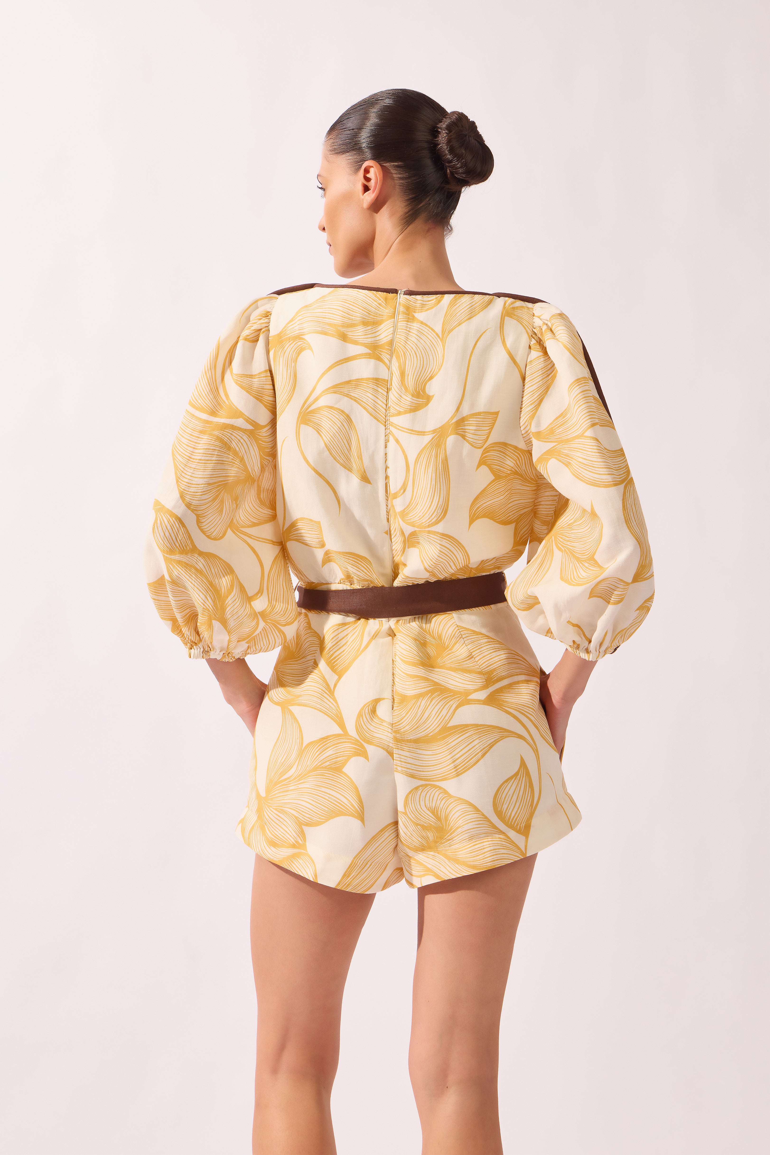 Model wearing the Foliage Romper back color cashew yellow, made from 55% linen 45% viscose, styled for a resort look