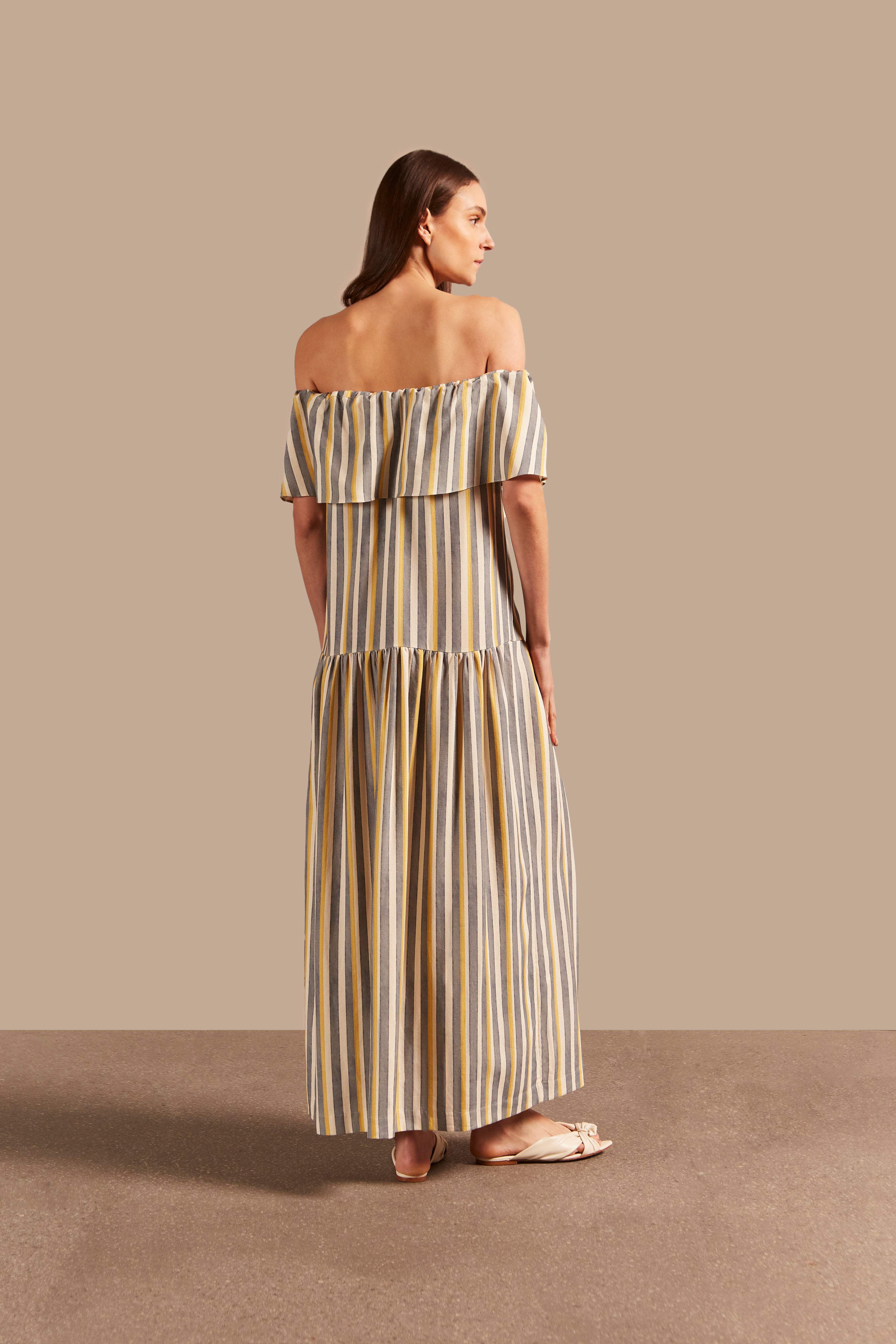 Model wearing the  Golden Age Off-The-Shoulder Long Dress showcasing the back of its vintage references with off white, blue and yellow print on a modal and linen fabric.