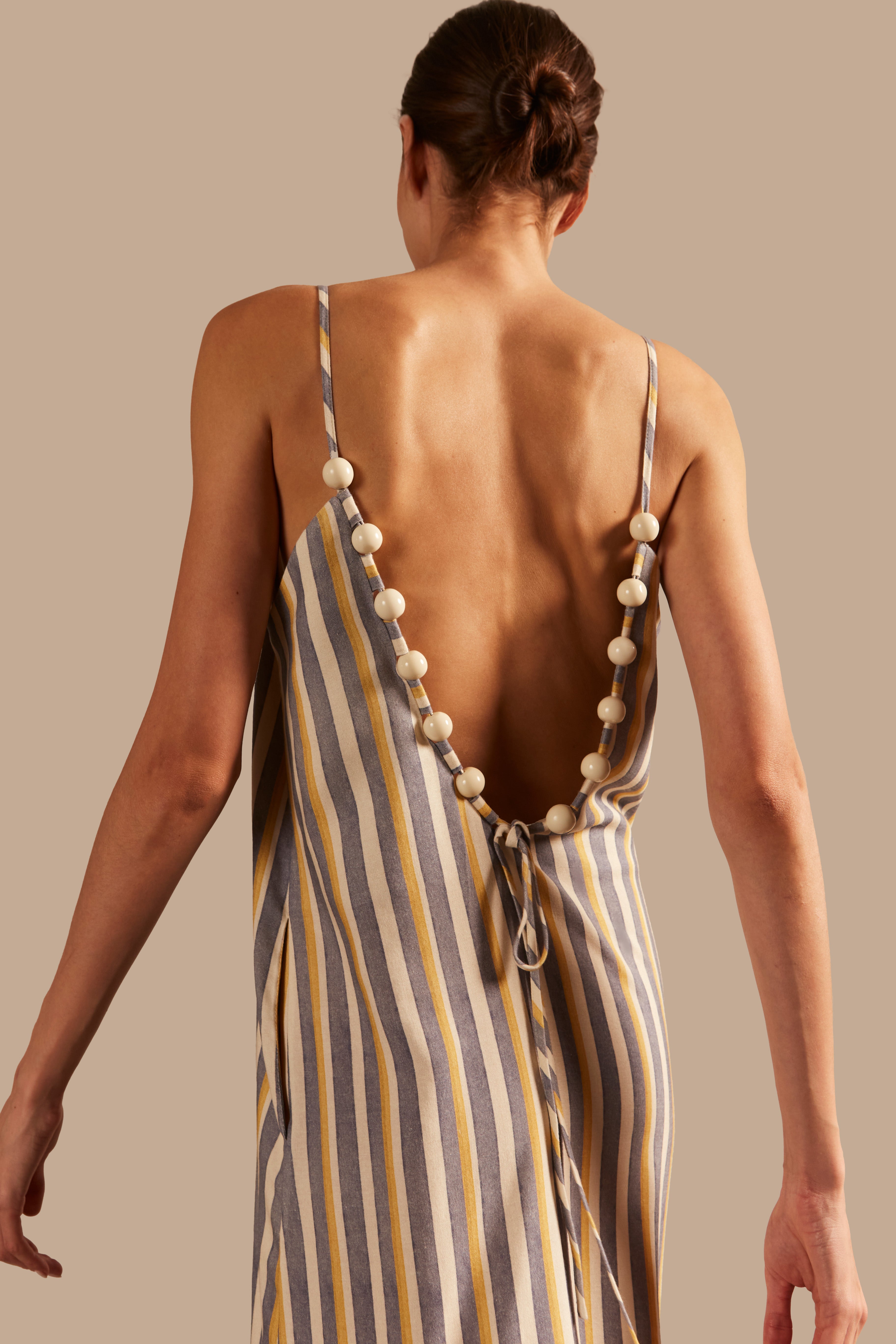 Model wearing the Golden Age Straps Long Dress showcasing the back of it's vintage references on Grey, Off White and Yellow print, on a modal and linen fabric.