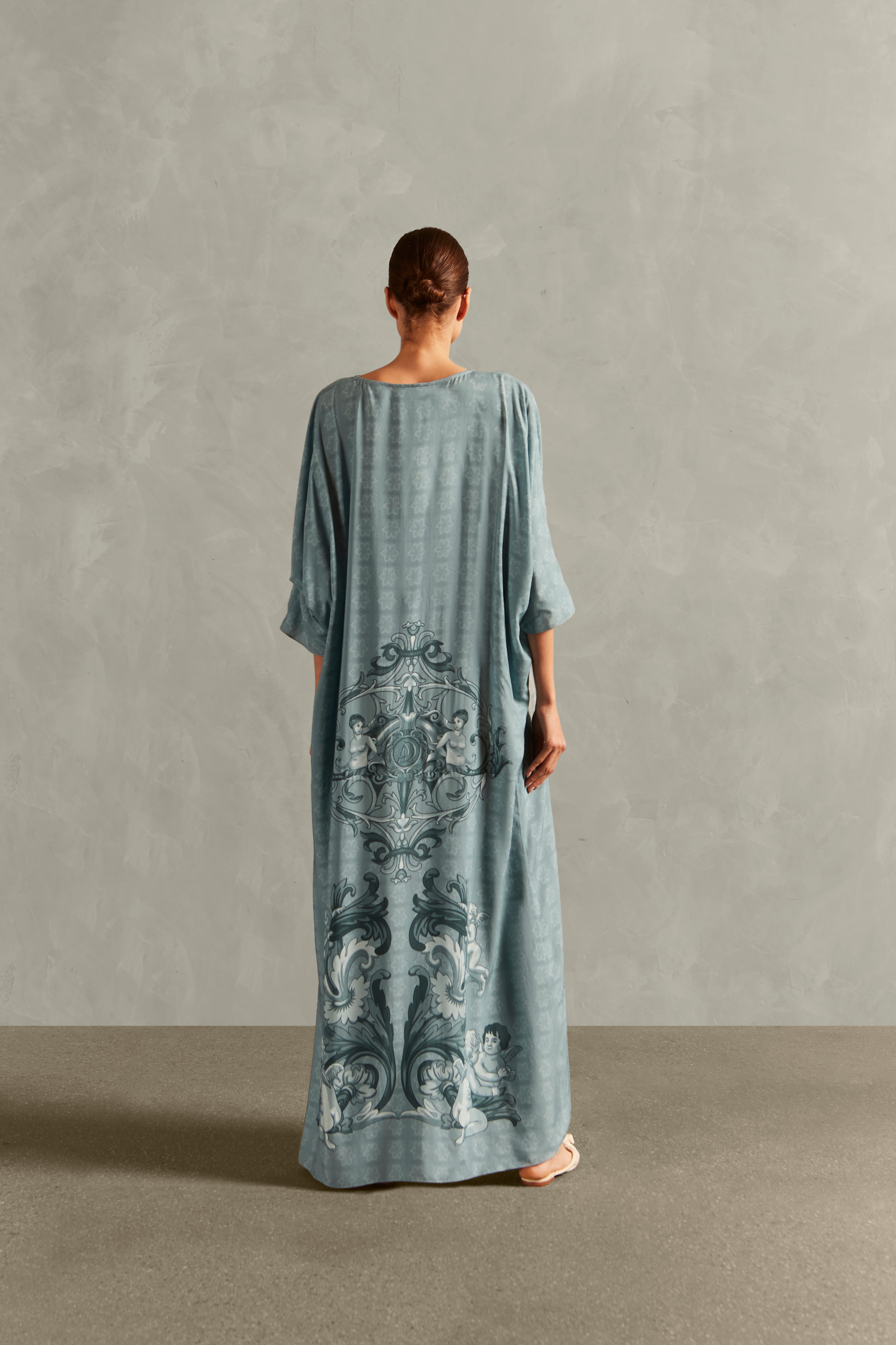 Model wearing the Hera Buttoned Long Robe Back showcasing its vintage references with Blue print on 100% Viscose fabric, styled for a resort look. 