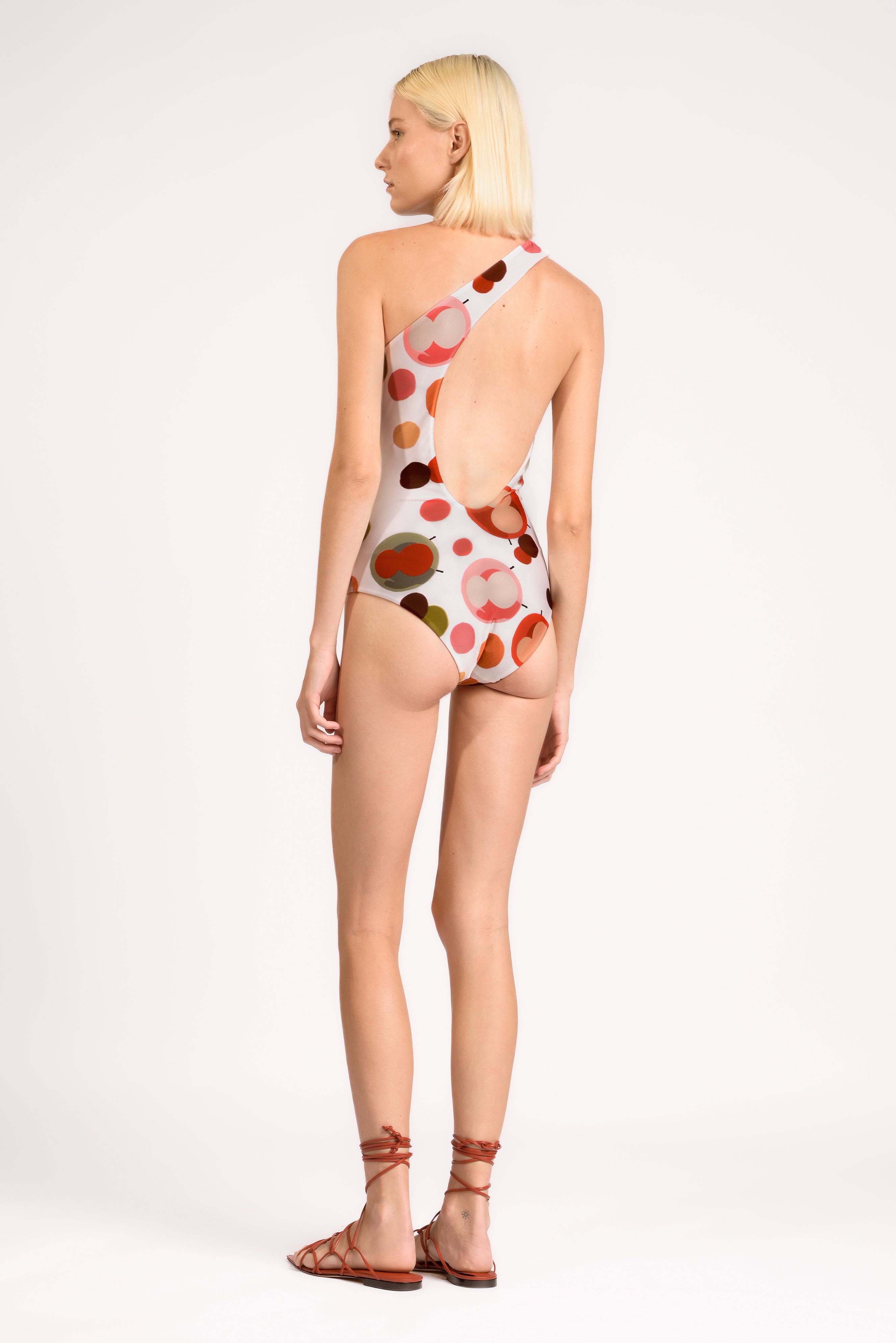 Model wearing the Lina One Shoulder Swimsuit detail back color unique, made from 85% polyester 15% elastane, styled for beachwear look 