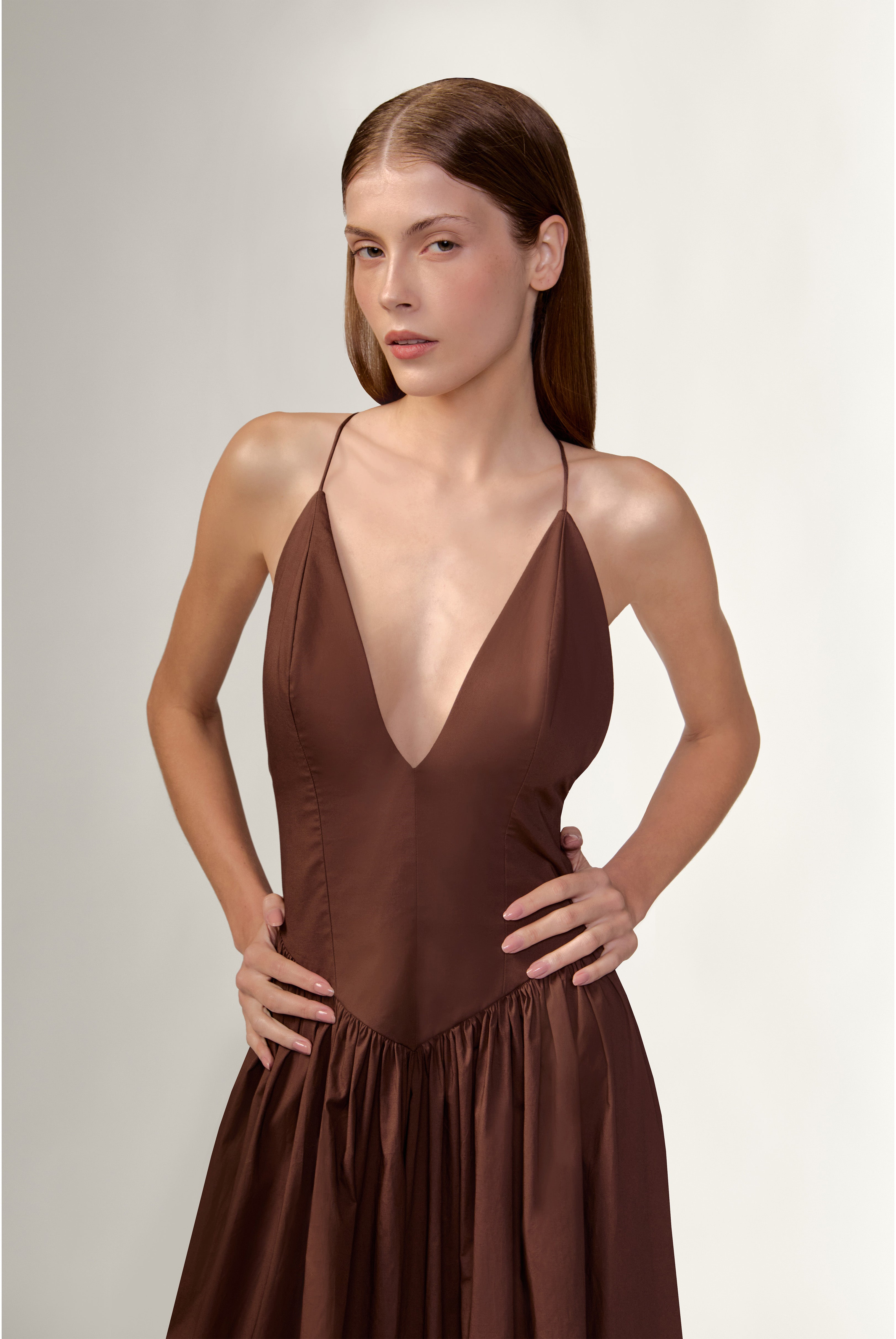 Model wearing the Opulence Deep V-Neck Maxi Dress detail color brown made with 97% Cotton 3% Elastane,  styled for a dinner look 