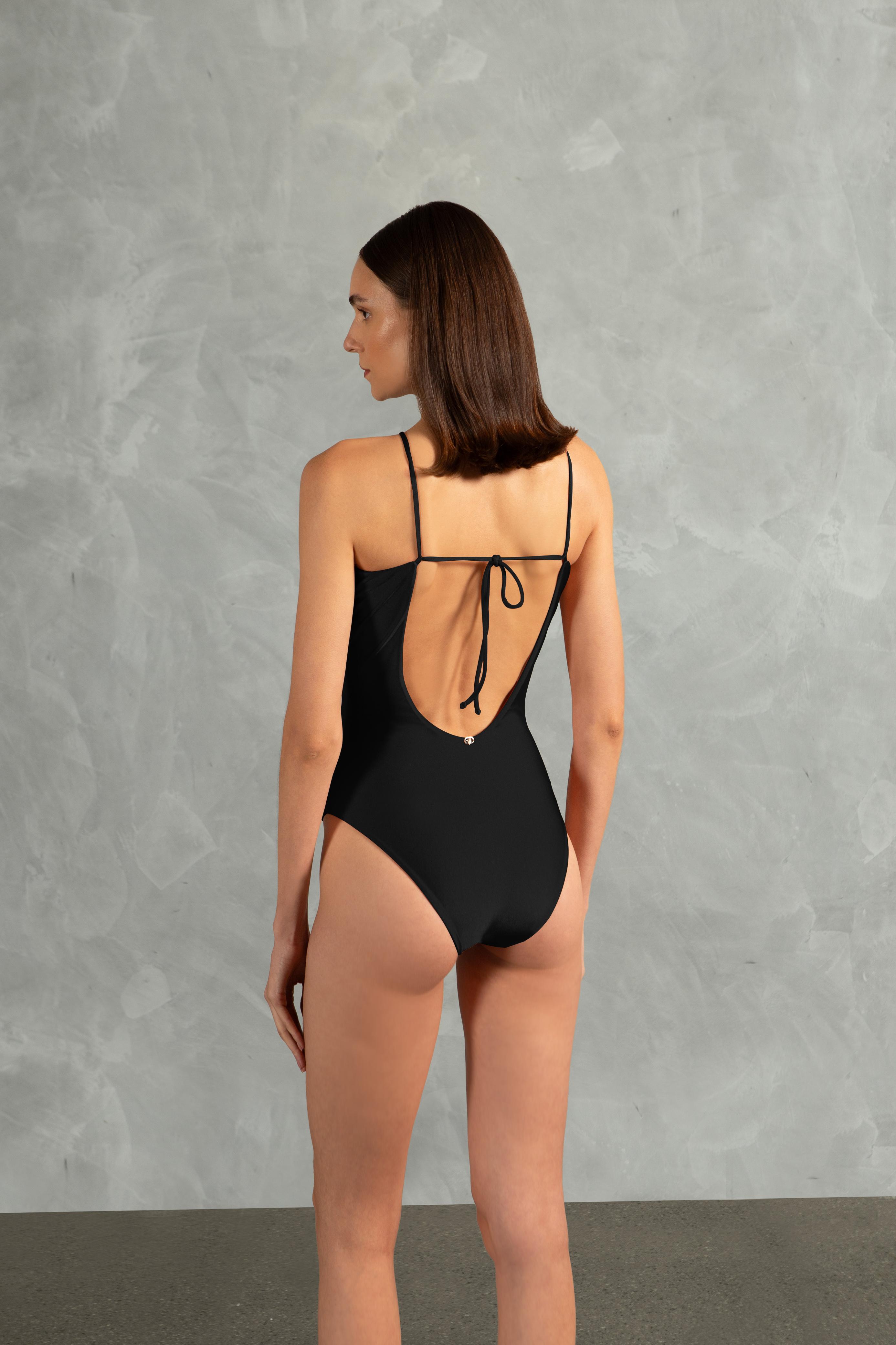 Model wearing the Oysters Solid Cut-Out Swimsuit With Pearls Back showcasing its Black print with Cut-outs and Pearls Applications on 85% polyamide 15% spandex fabric, styled for a beachwear look.