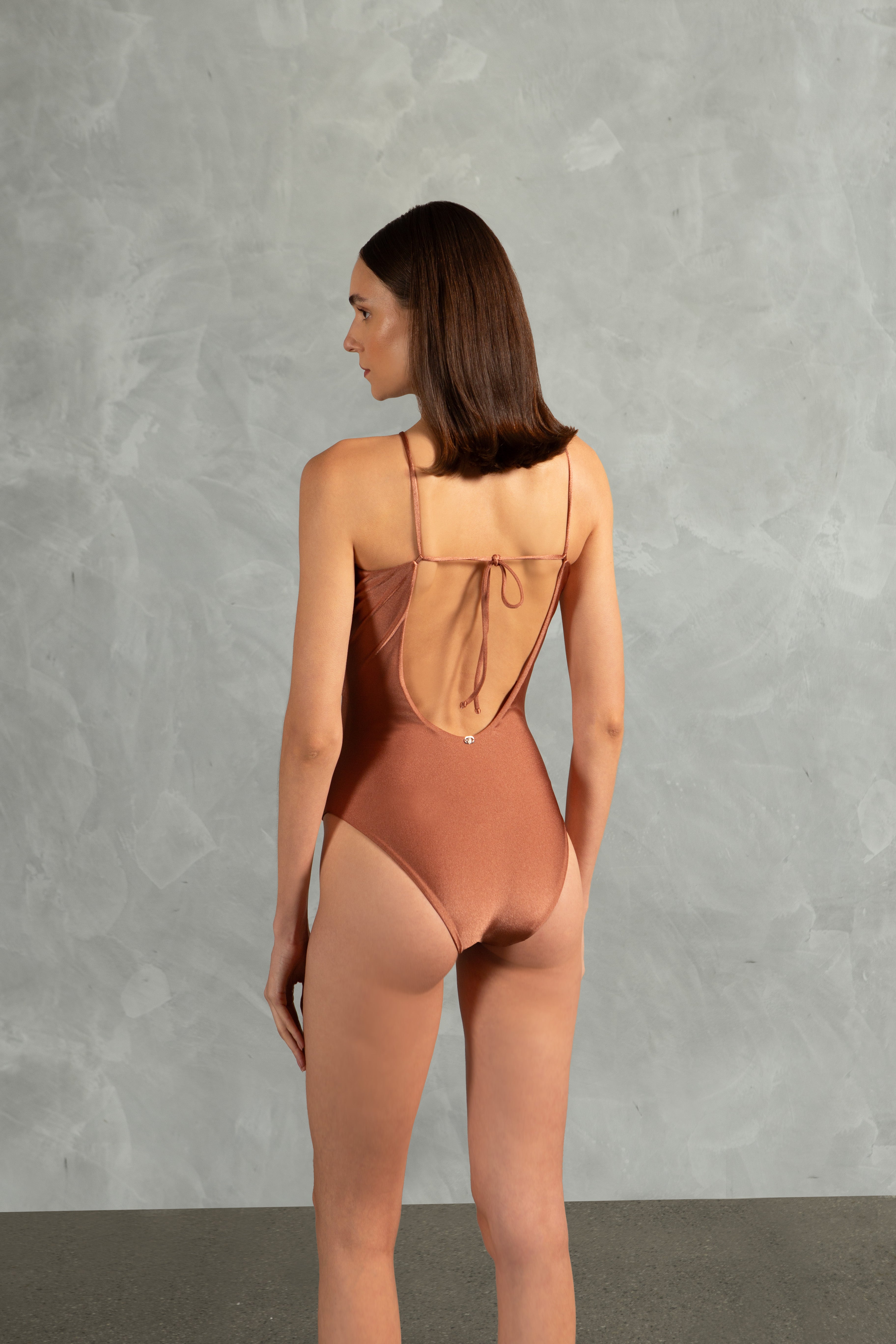 Model wearing the Oysters Solid Cut-Out Swimsuit With Pearls Back showcasing its Light Brown print with Cut-outs and Pearls Applications on 85% polyamide 15% spandex fabric, styled for a beachwear look.