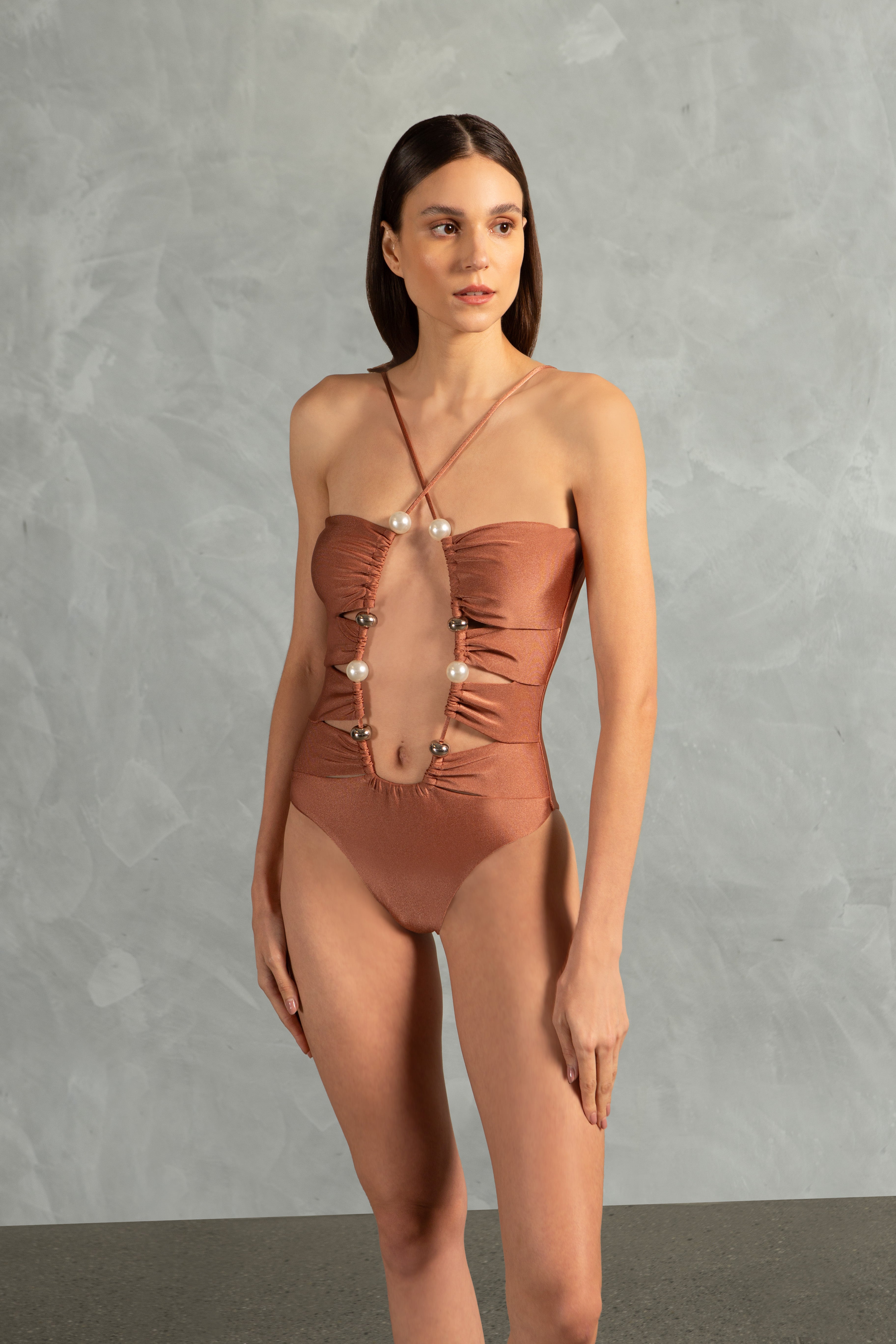 Model wearing the Oysters Solid Cut-Out Swimsuit With Pearls Close showcasing its Light Brown print with Cut-outs and Pearls Applications on 85% polyamide 15% spandex fabric, styled for a beachwear look.