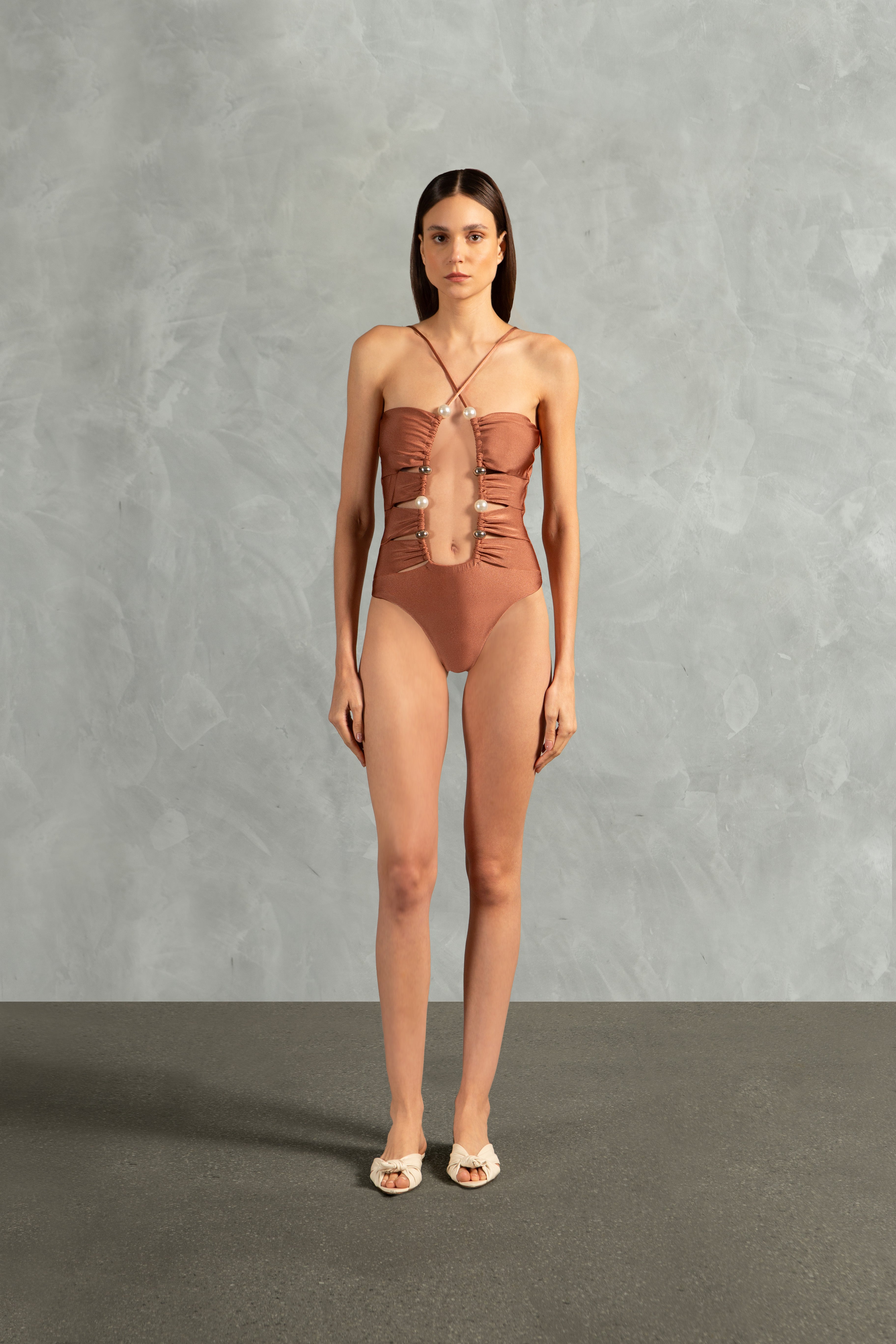 Model wearing the Oysters Solid Cut-Out Swimsuit With Pearls Front showcasing its Light Brown print with Cut-outs and Pearls Applications on 85% polyamide 15% spandex fabric, styled for a beachwear look.