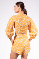 Model wearing the Polka Dots Shorts back color cashew yellow, made from 55% linen 45% viscose, styled for a resort look