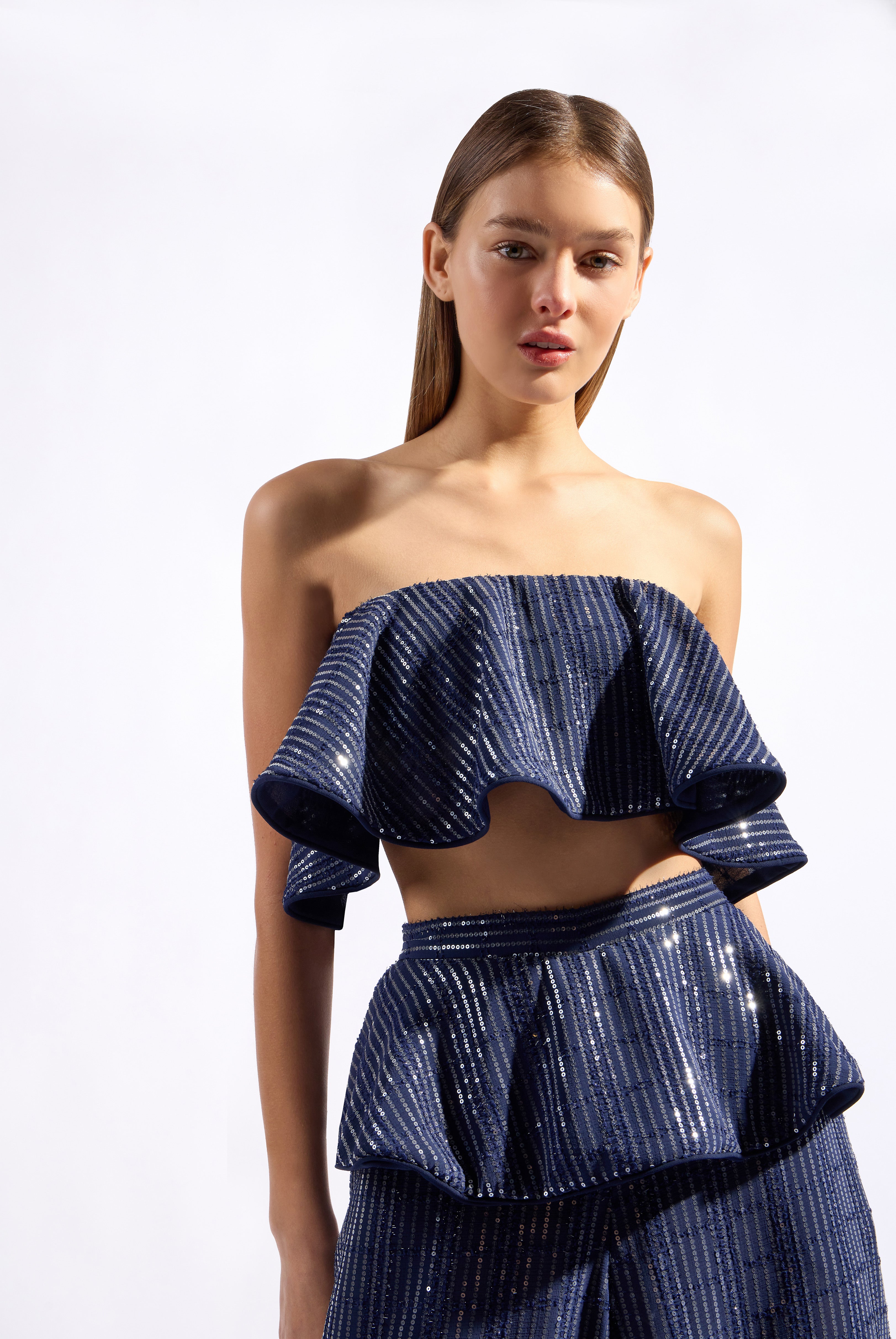 Model wearing the Sequin Ruffled Crop Top color navy made from 100% polyester fabric, styled for a resort look