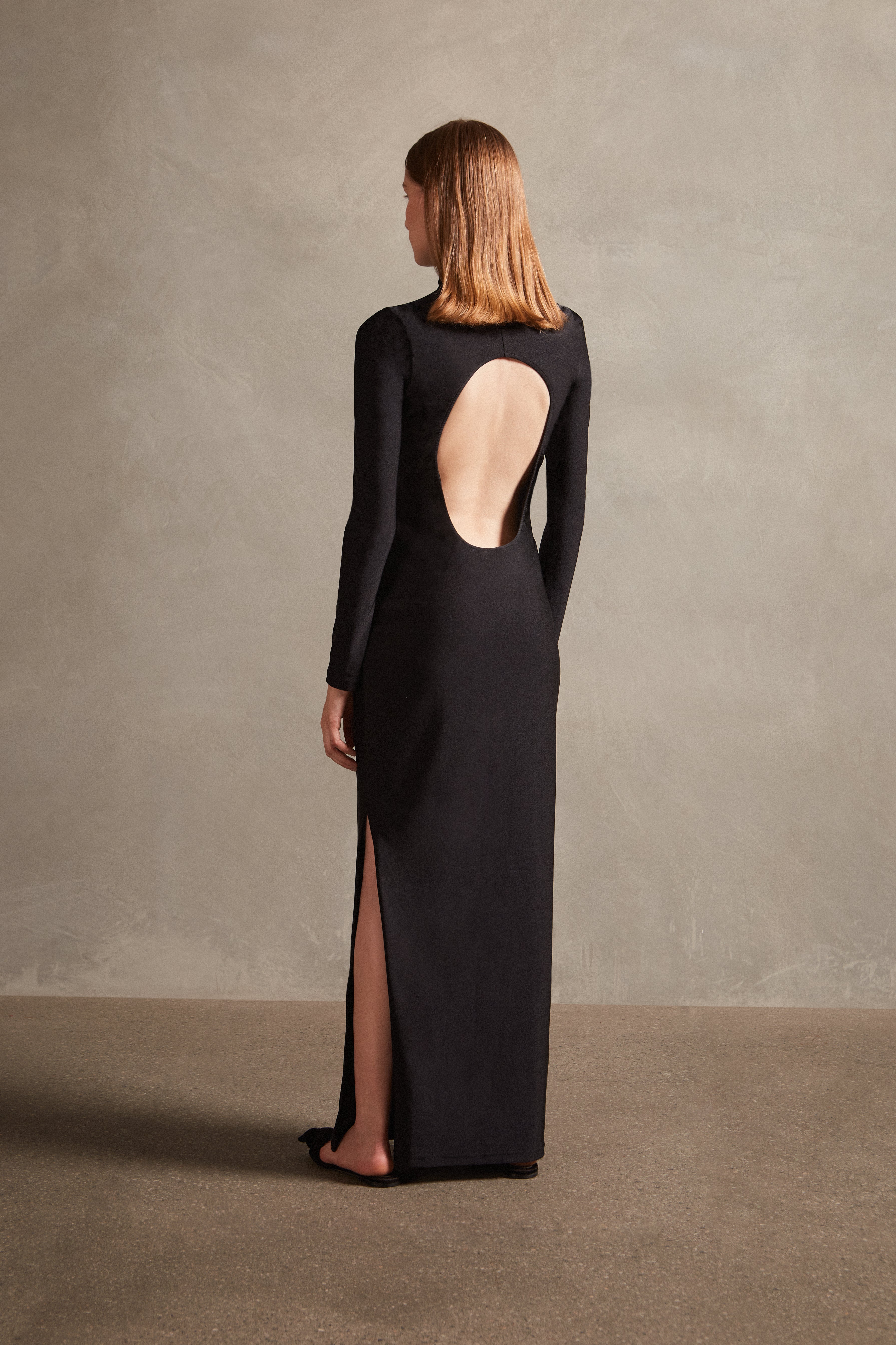 Model wearing the Solid Open Back Long Dress back showcasing the timeless piece, with black print, on 85% polyamide 15% spandex fabric.