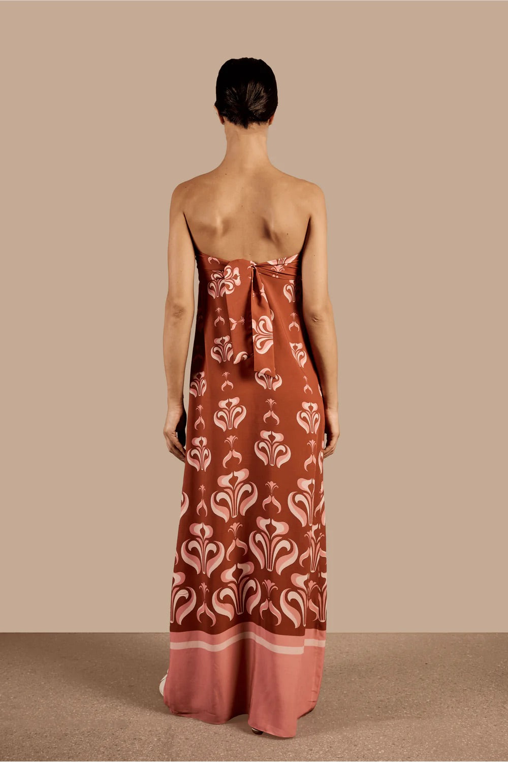 Model wearing the Vintage Lily Long Dress With Knot Detail showcasing the back of it's strapless design, with dark red and pink print, on a viscose fabric.