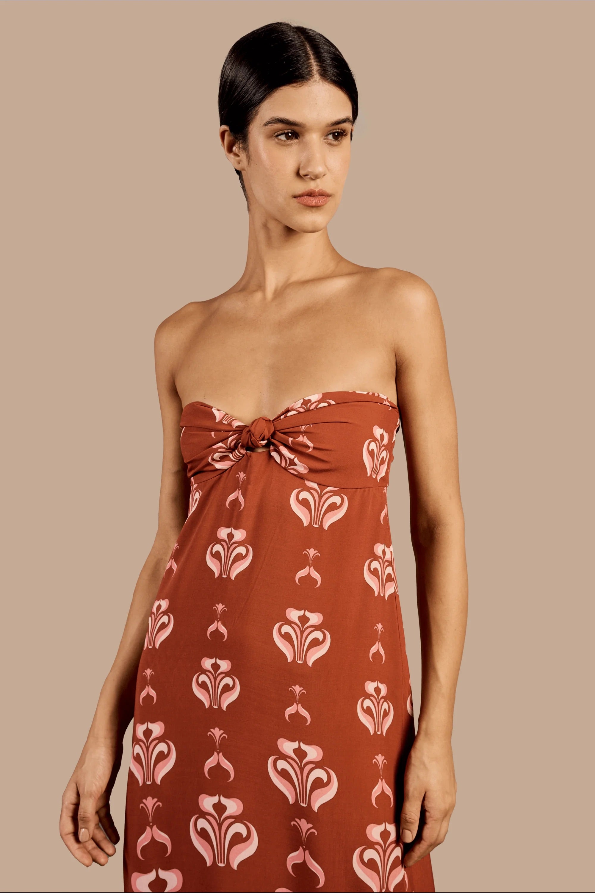 Model wearing the Vintage Lily Long Dress With Knot Detail showcasing the close up of it's strapless design, with dark red and pink print, on a viscose fabric.