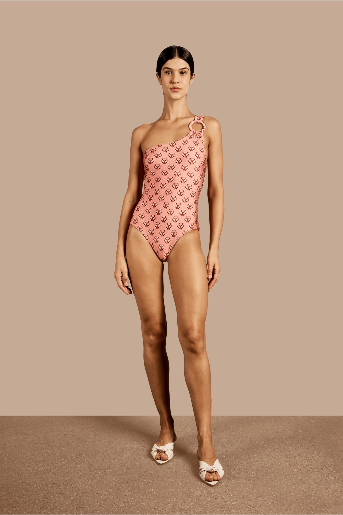 Model wearing the Vintage Lily One-Shoulder Swimsuit With Hoop showcasing the front of it's asymmetrical model, with a pink print, on a stretchy fabric.