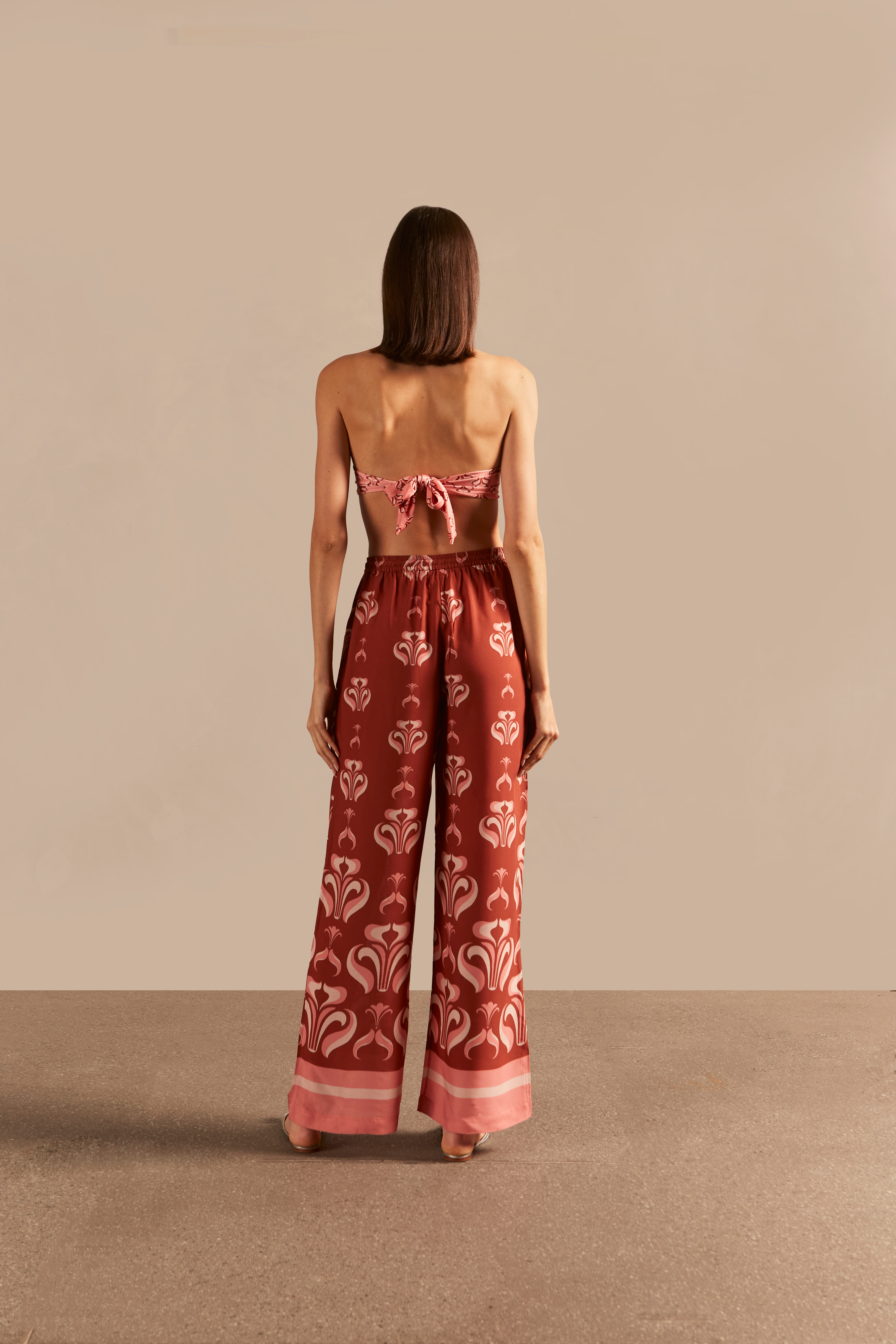 Model wearing the Vintage Lily Wide-Leg Pants showcasing the back of it's vintage inspired dark red and pink print, on a viscose fabric.