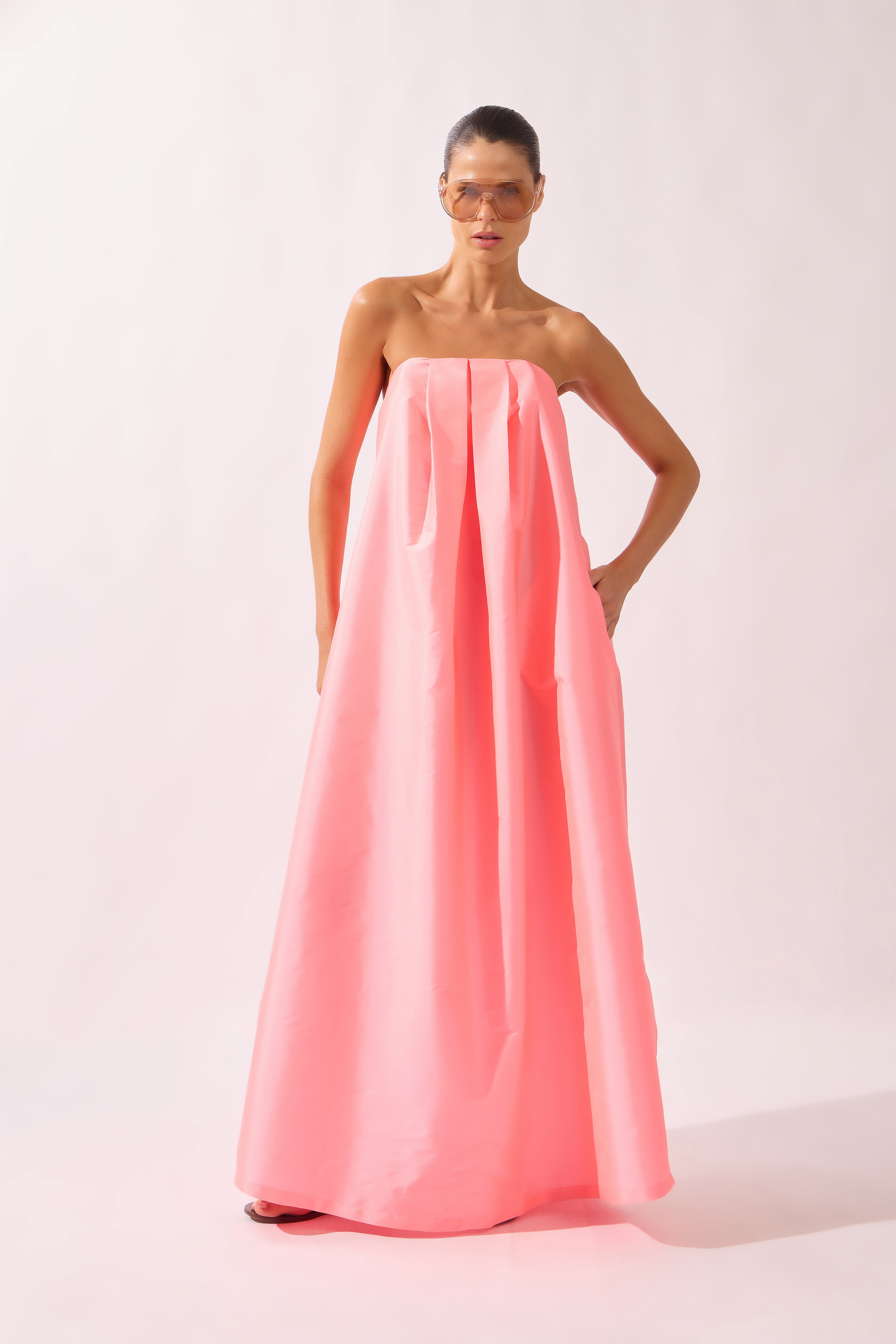 Model wearing the Voluminous Maxi Dress front color flourescent pink made with 100% polyetser, styled for an evening look