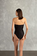 Model wearing the Waves Strapless Swimsuit Back showcasing its Black color on 85% Polyamide 15% Elastane fabric, styled for a beachwear look. 
