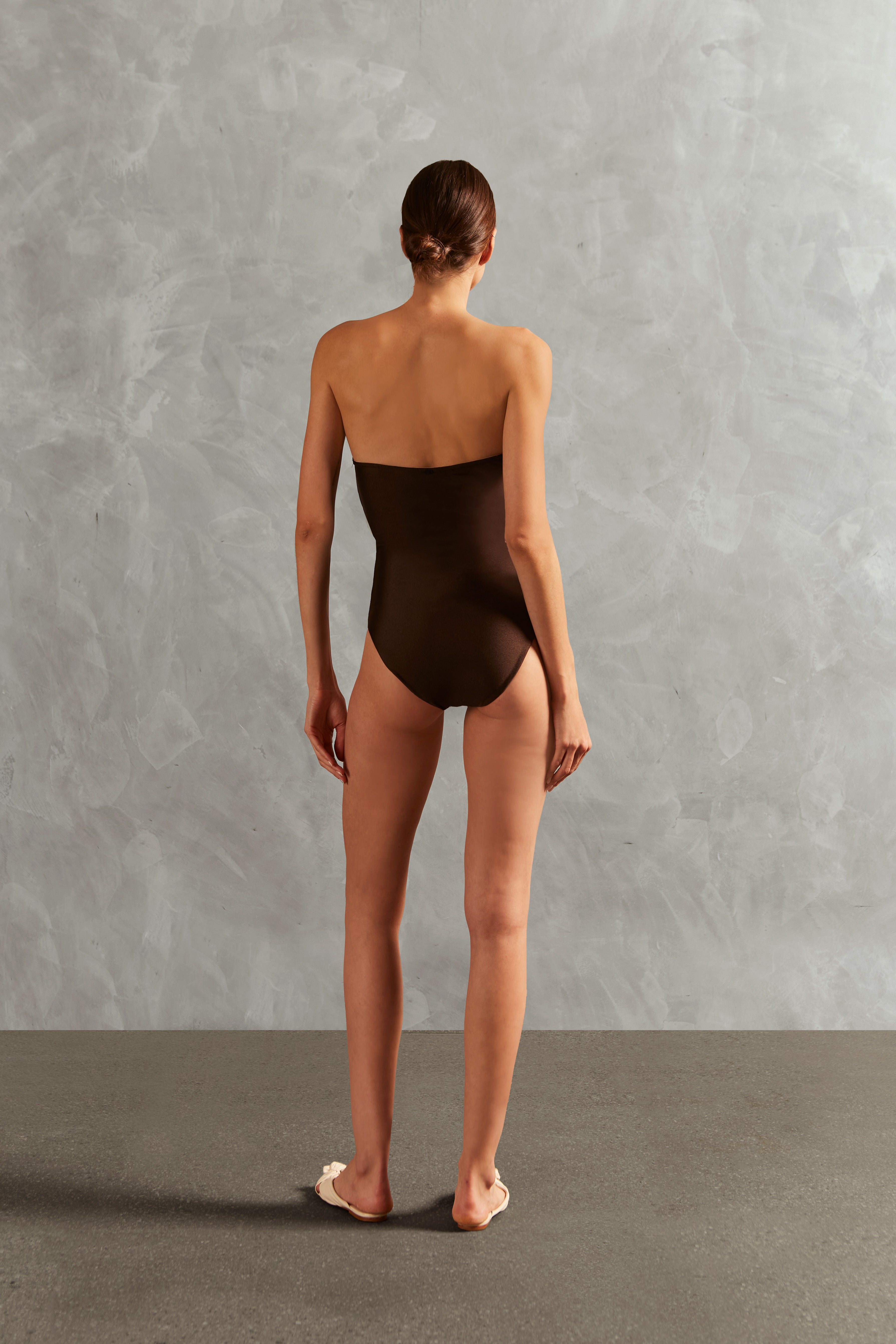 Model wearing the Waves Strapless Swimsuit Back showcasing its Coffee color on 85% Polyamide 15% Elastane fabric, styled for a beachwear look. 